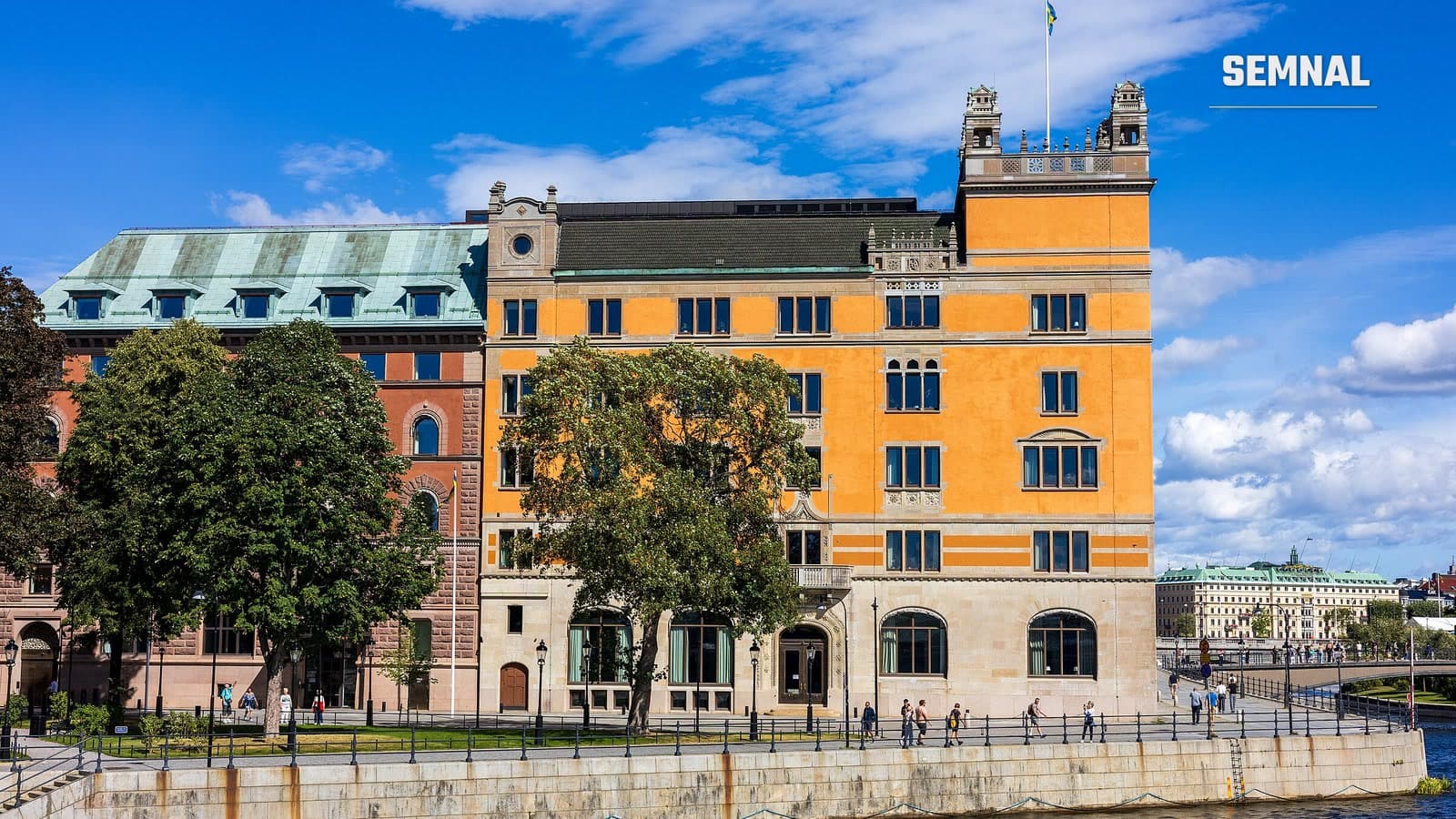 Clădirea Rosenbad din Stockholm, sediul guvernului suedez, cu fațada portocalie și drapelul Suediei pe acoperiș, văzută de pe malul apei