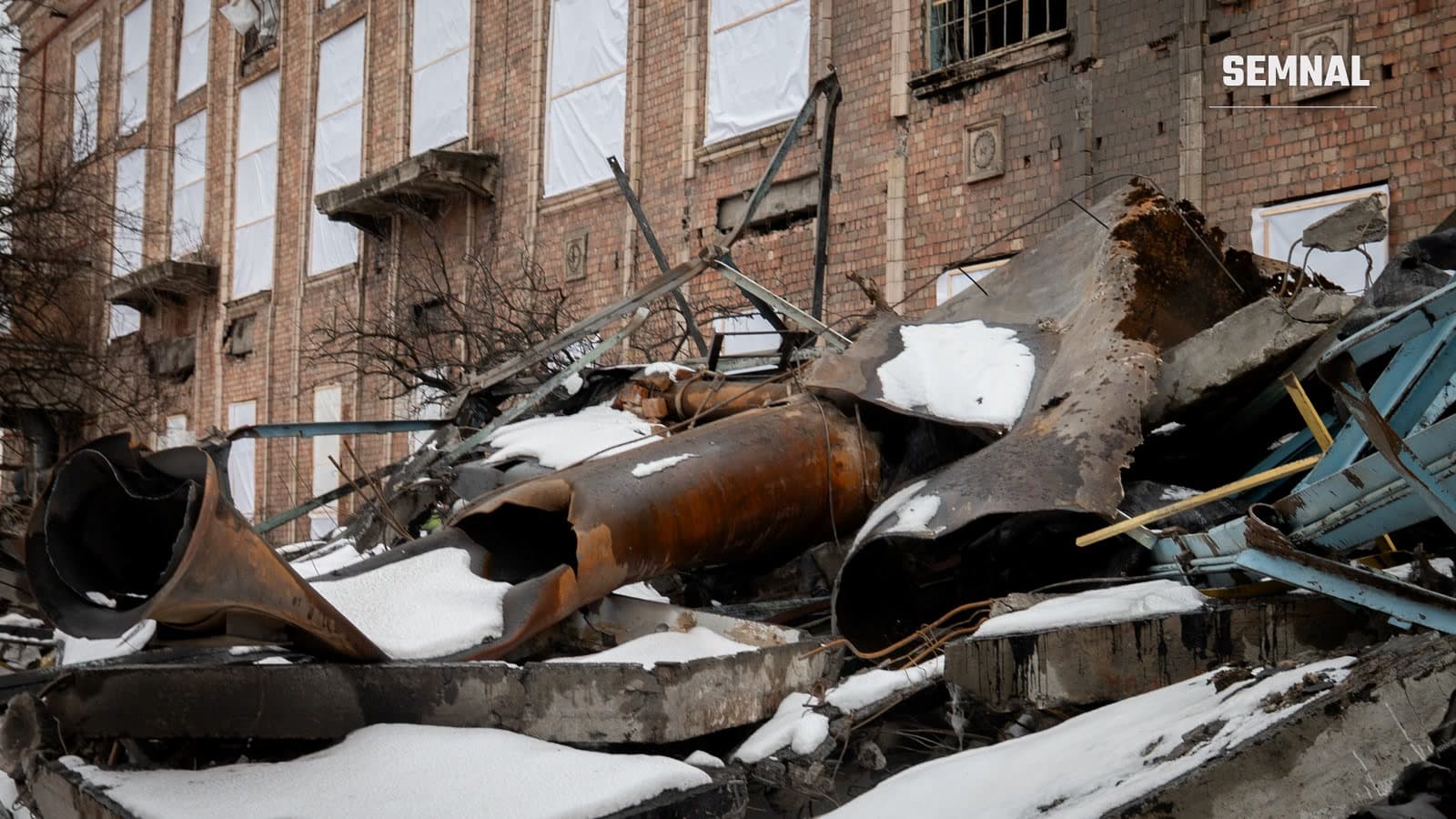 Țevi metalice ruginite și dărâmături acoperite de zăpadă în fața clădirii de cărămidă a centralei termice Darnîțka din Kiev, avariată de un atac rusesc în februarie 2026. (Foto: Ministerul pentru Dezvoltarea Comunităților și Teritoriilor al Ucrainei / Wikimedia Commons, CC BY 4.0)