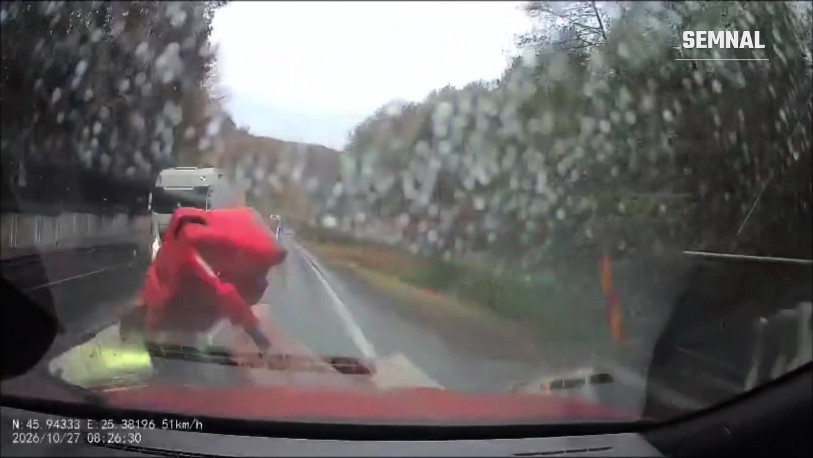 Baliză roșie lovind parbrizul unei mașini pe DN 13, pe ploaie, în timp ce un camion vine din sens opus