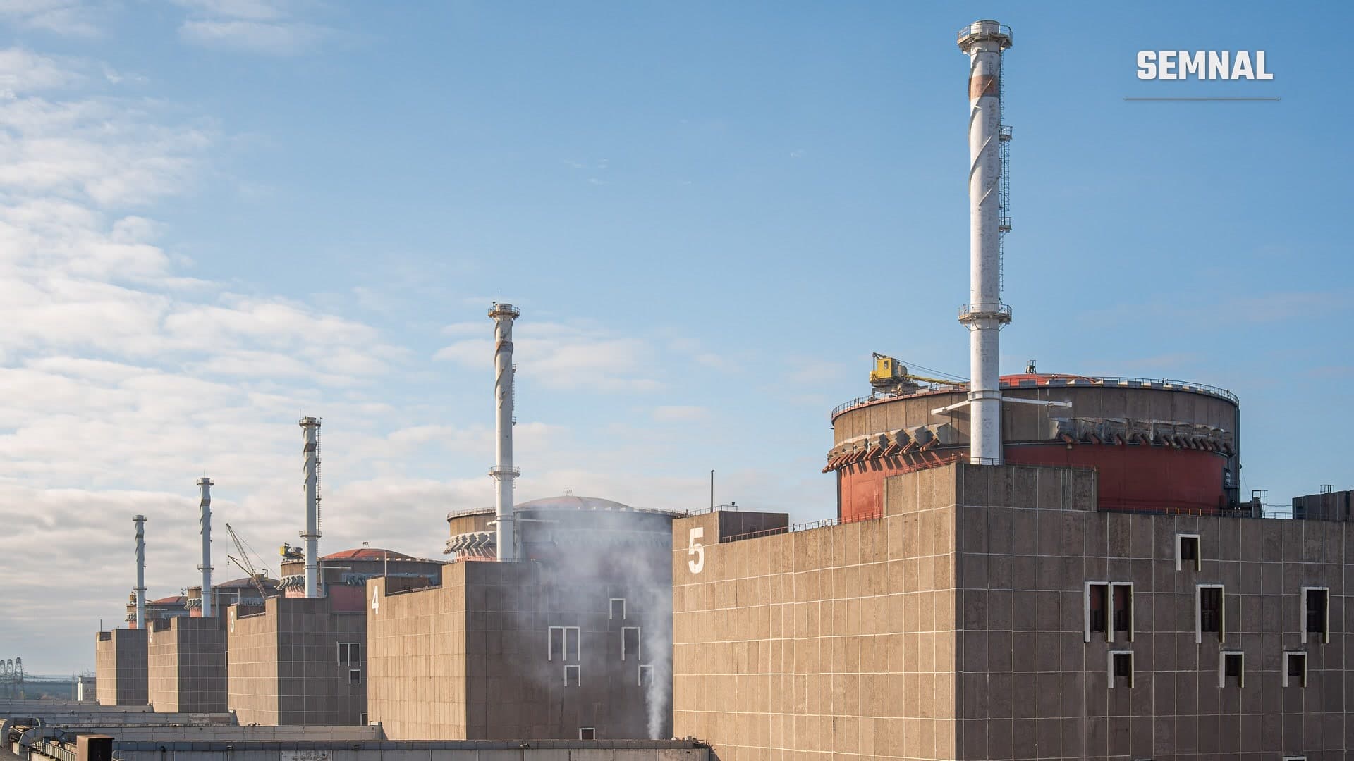 Coșuri de fum înalte și clădirile cenușii ale reactoarelor centralei nucleare de la Zaporojie, sub un cer albastru cu nori ușori, într-o fotografie de arhivă din 2021