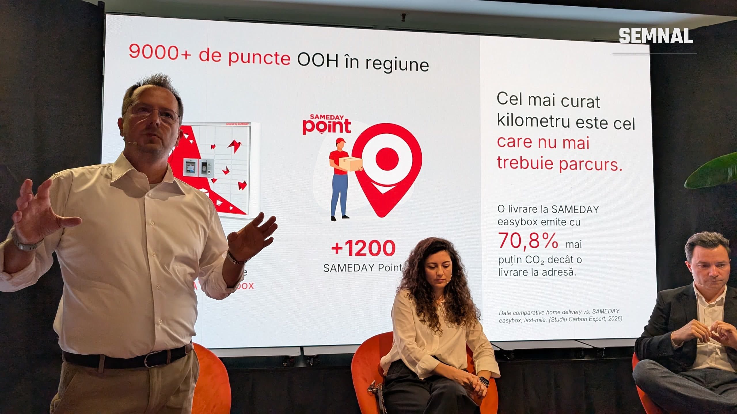 Lucian Baltaru, CEO SAMEDAY, vorbește pe scenă în fața unui ecran despre rețeaua easybox, cu Elena Stoica și Alexandru Niculescu așezați în fotolii. Fotografie realizată de Lucian Dinu