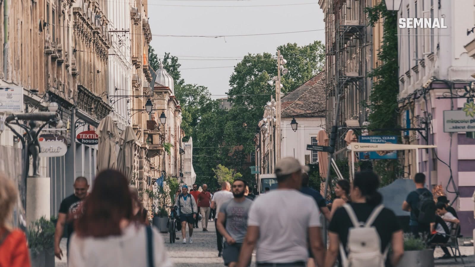 Stradă pietonală aglomerată din centrul istoric al Timișoarei, cu clădiri de epocă, felinare și pietoni în timpul zilei