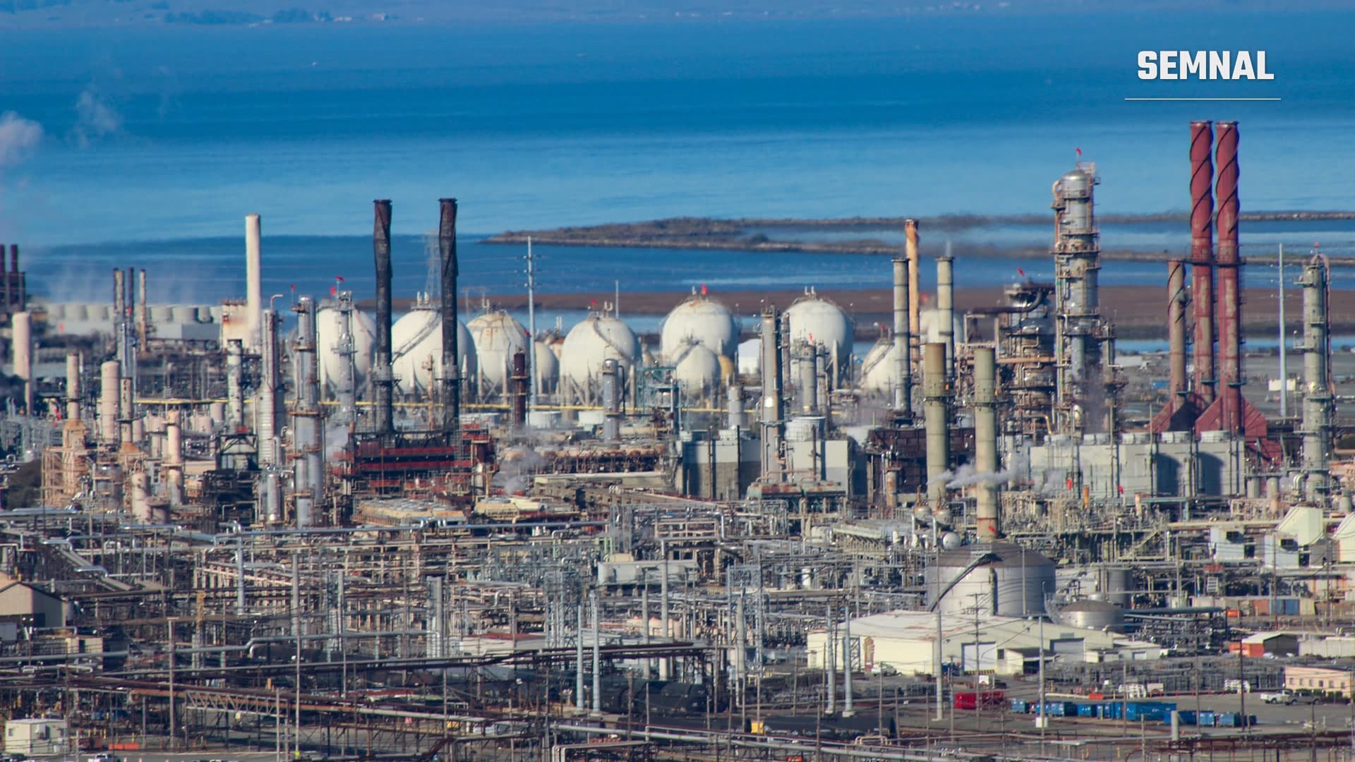 Rafinăria Chevron din Richmond, California, cu coloane de distilare, coșuri și rezervoare sferice, pe fundalul golfului San Pablo