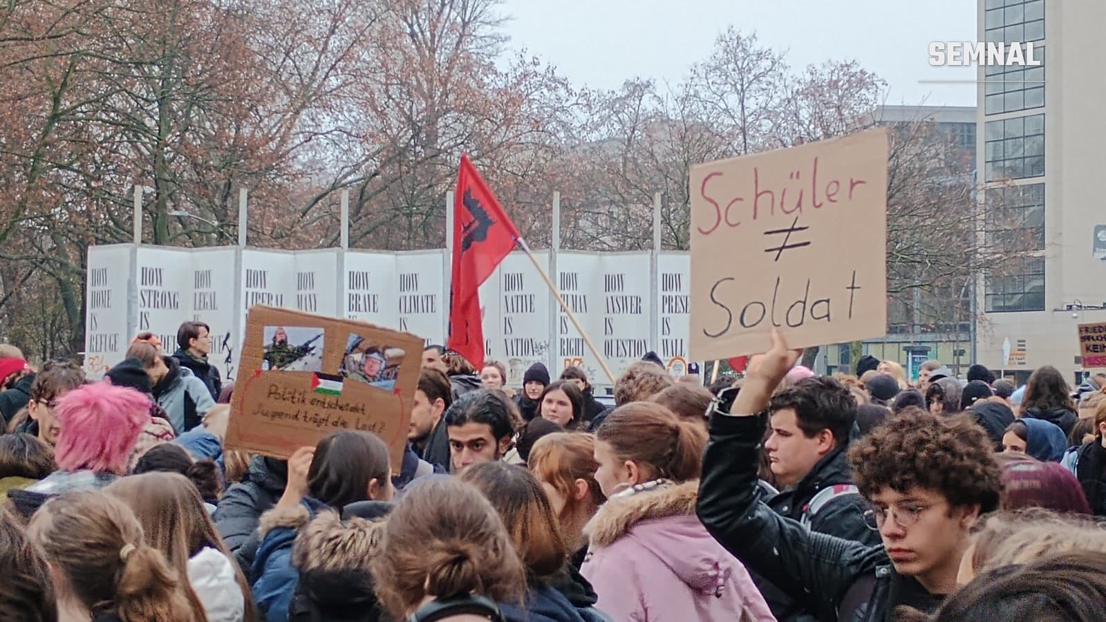 Elevi și tineri la un protest la Berlin, unul dintre ei ridicând o pancartă din carton pe care scrie „Schüler ≠ Soldat”