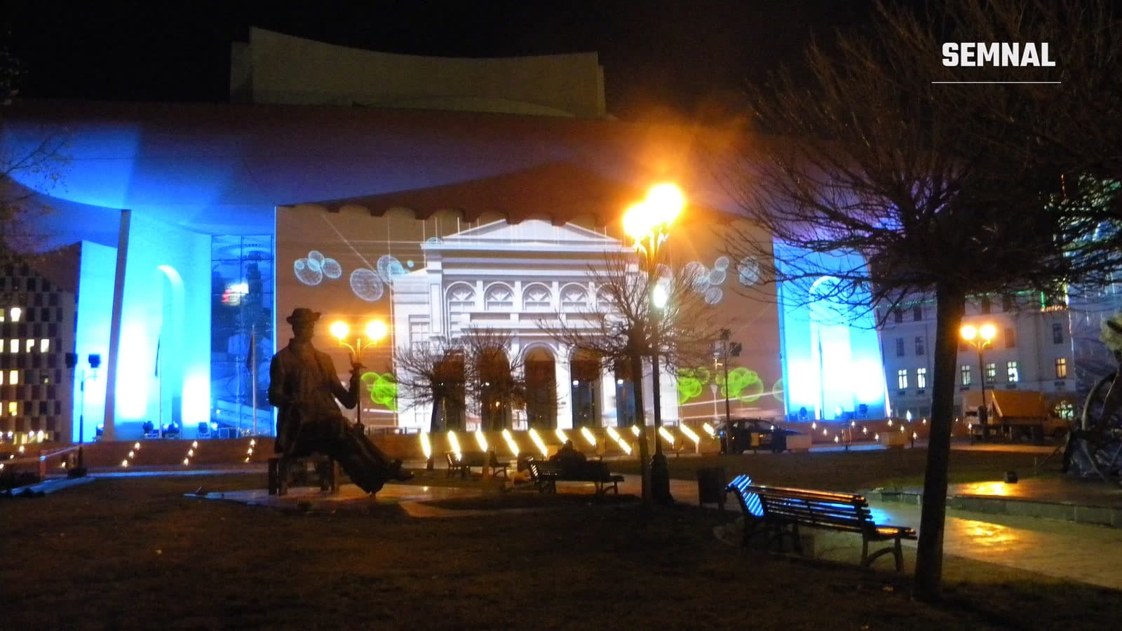 Clădirea Teatrului Național din București luminată noaptea, cu statuia lui I.L. Caragiale în prim-plan