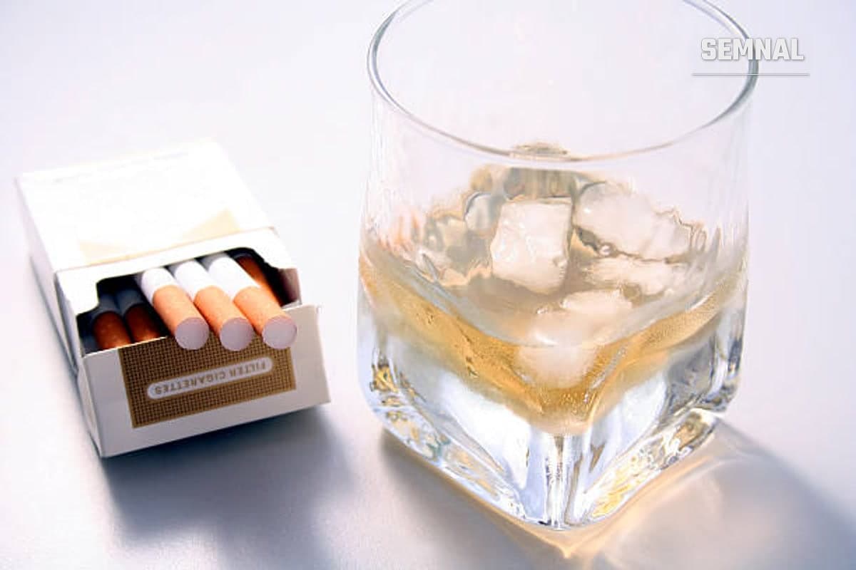 In imagine este un pahar cu alcool și cuburi de gheață, alături de un pachet de țigari desfăcut.