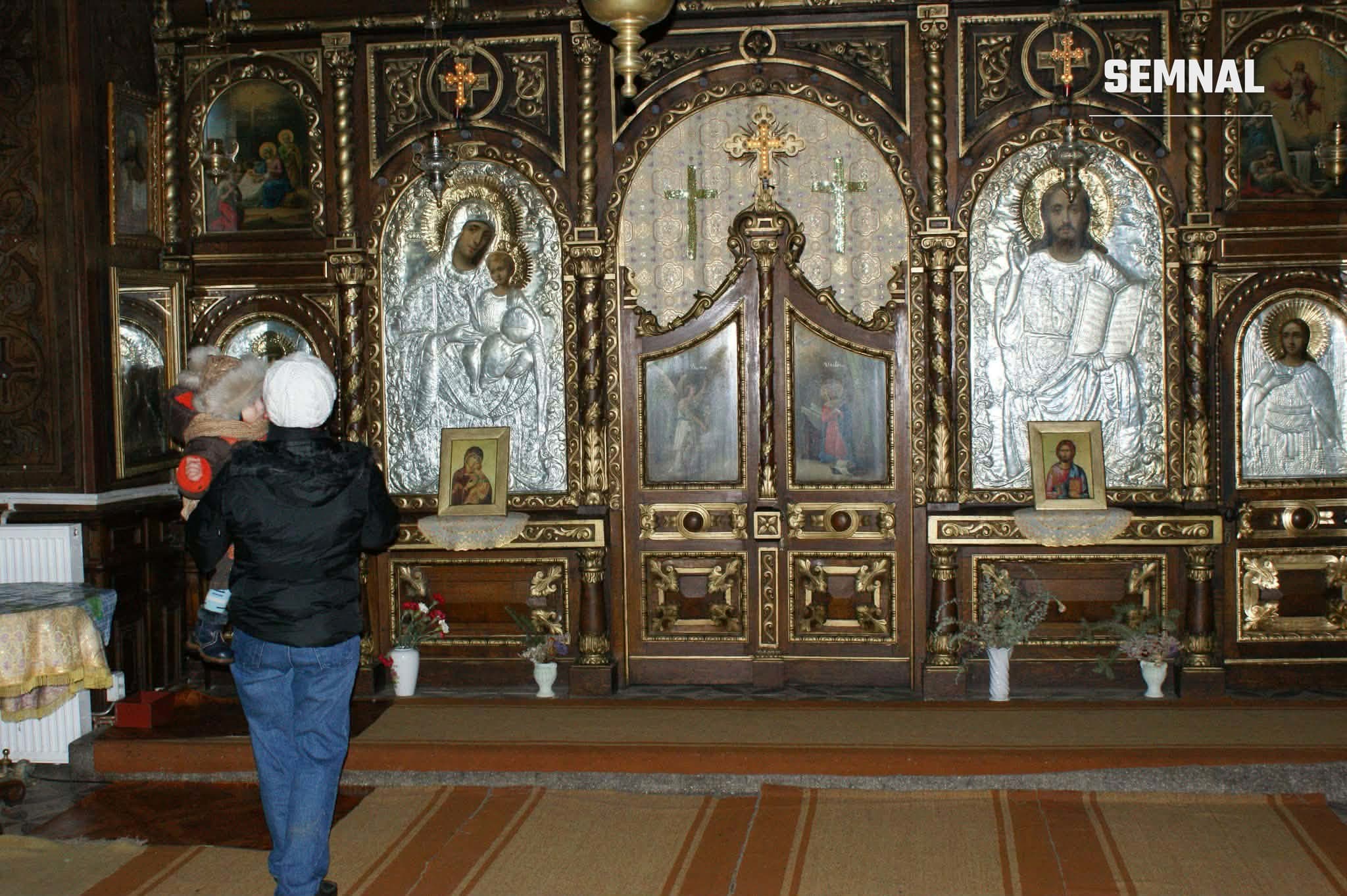 În imagine este un interior de biserică ortodoxă cu o mamă și un copil.
