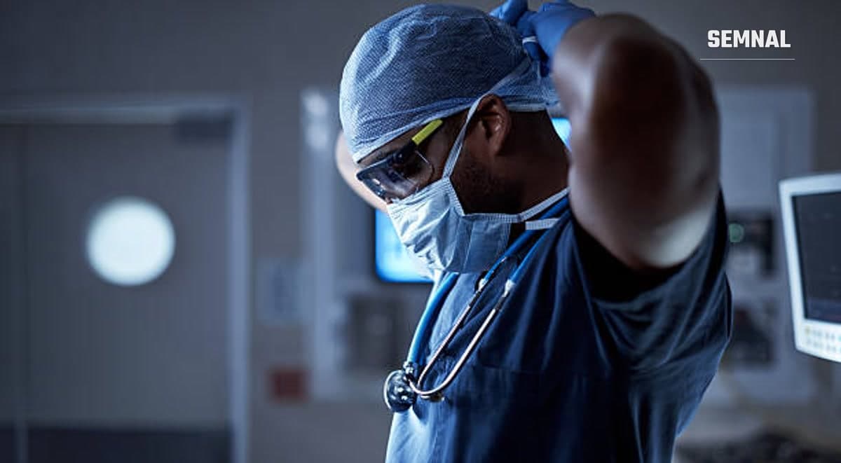 În imagine este un asistent medical care își pune masca de protecție la gură.