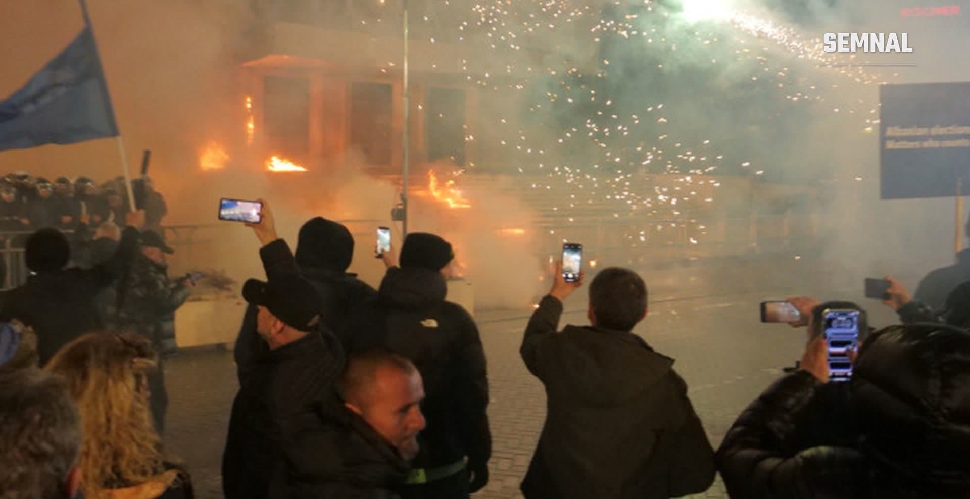 În imagine sunt mai mulți protestatari din Tirana, care filmează cu telefoanele explozii și incendii.
