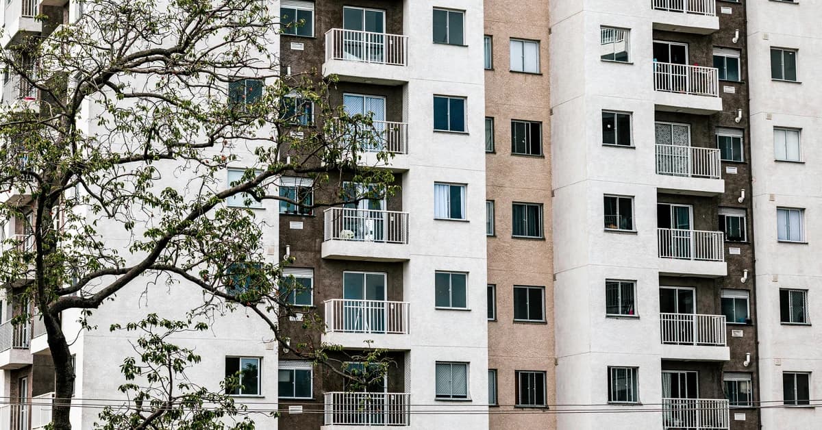 Bloc de apartamente cu mai multe etaje, balcone și ferestre, înconjurat de copaci sub cer înnorat.