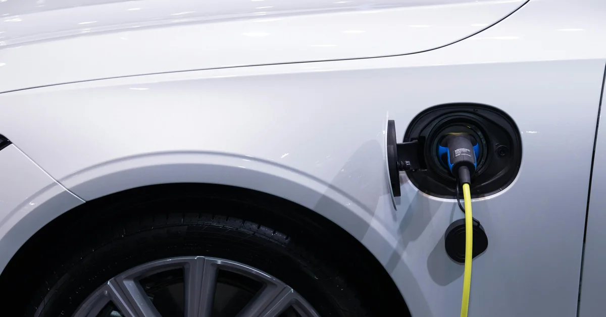 O mașină electrică albă cu portul de încărcare deschis și cablul de încărcare conectat.