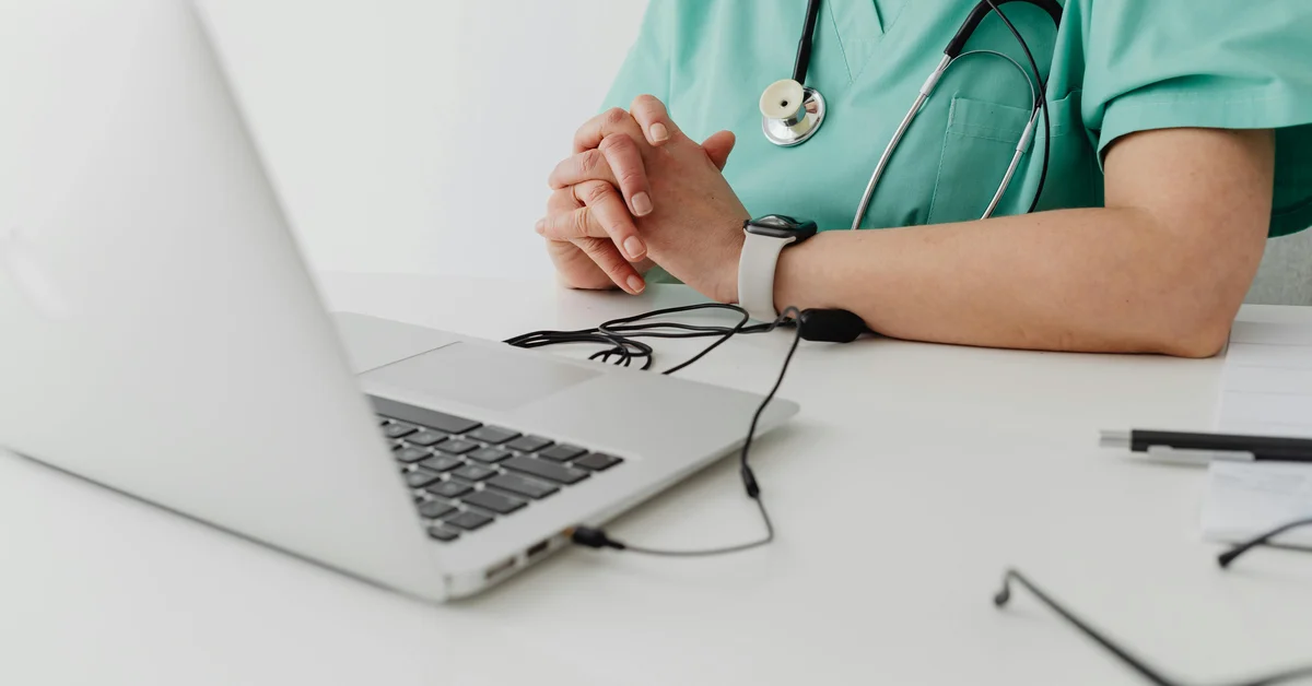Asistentă medicală în uniformă verde lucrează la un laptop, cu un stetoscop în jurul gâtului