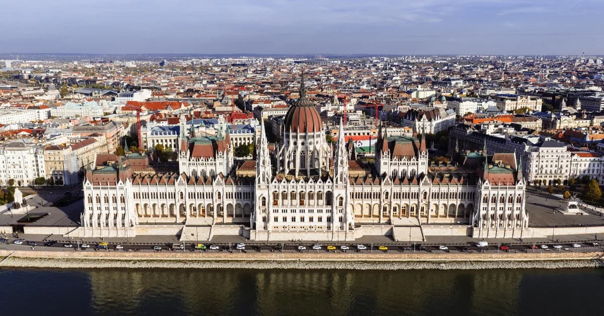 Clădirea Parlamentului din Budapesta văzută de sus, lângă râul Dunărea, cu orașul în fundal și cer senin.