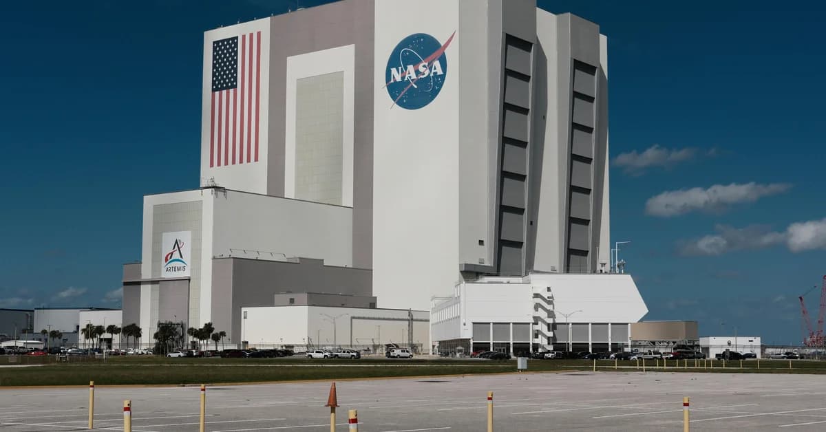 Clădire mare NASA sub cer albastru, cu steagul SUA; parcare în față, câteva nori pe cer.