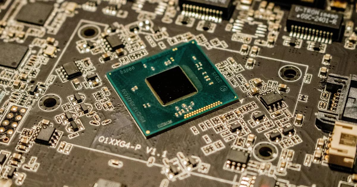 Placă de circuit imprimat cu un microcip albastru în centru, înconjurat de componente electronice.