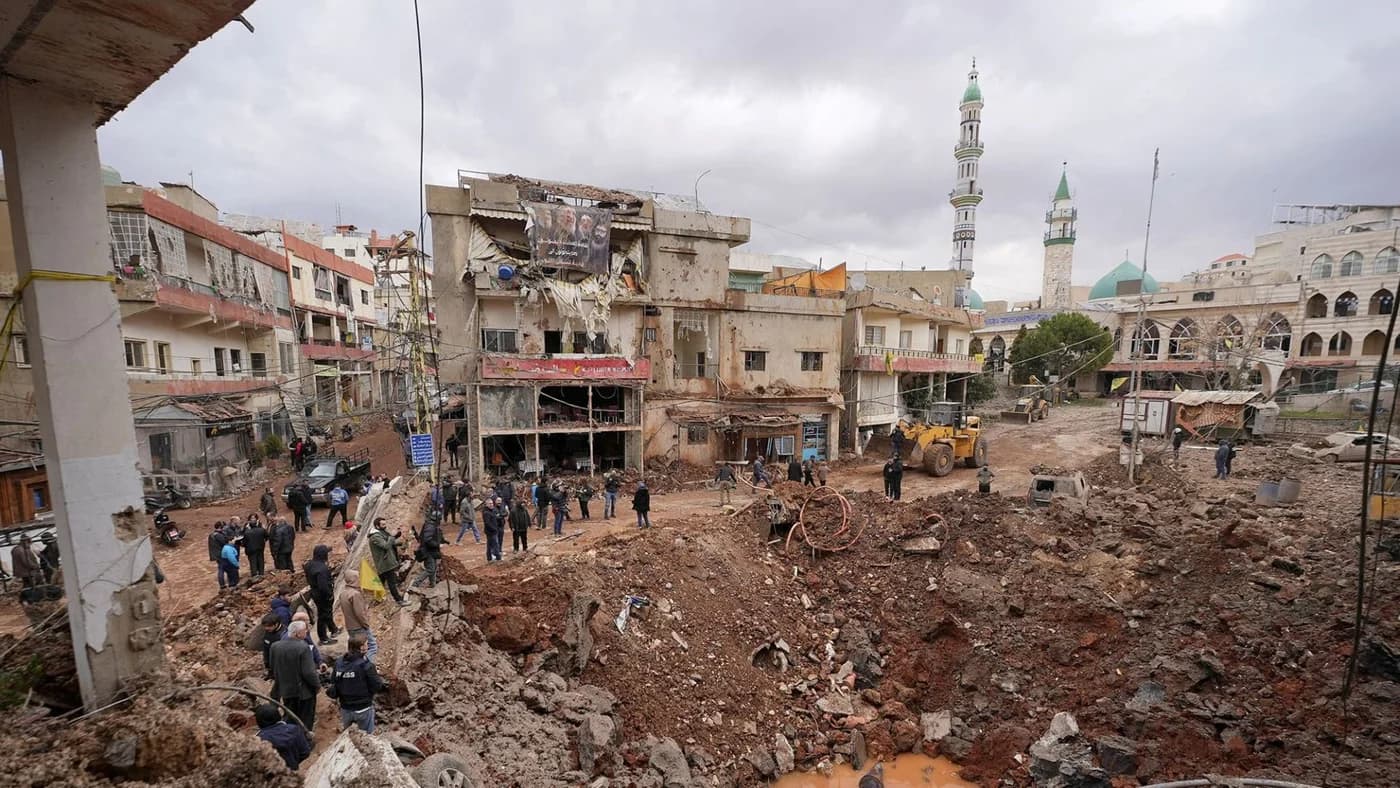 Zonă urbană devastată în Cisiordania cu clădiri distruse, oameni adunați printre ruine, excavator pentru demolări și minarete în fundal, ilustrând consecințele conflictului israeliano-palestinian.