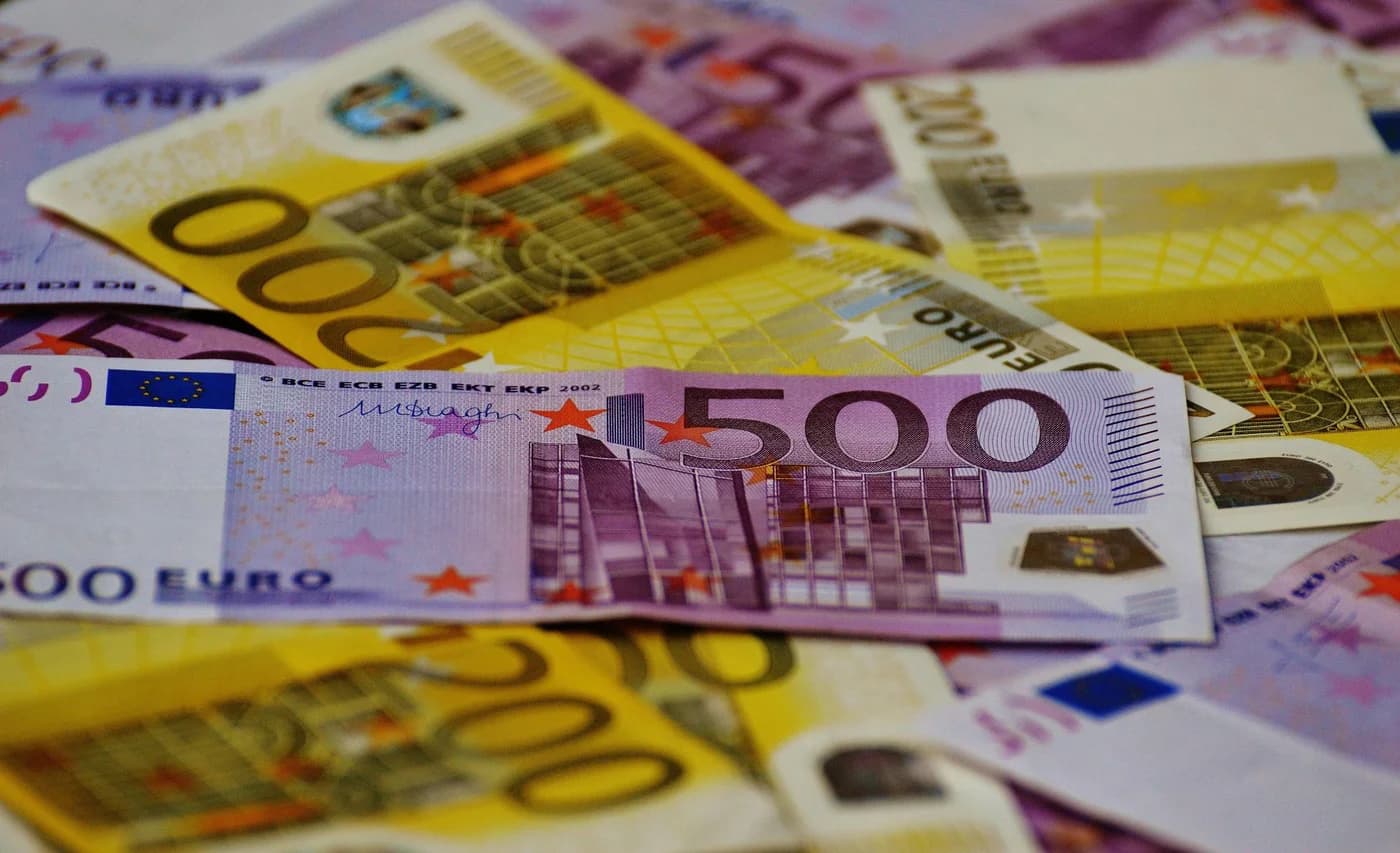 Bancnote euro de 500 și 100 de euro suprapuse și aranjate pe o suprafață, reprezentând transfer de fonduri și finanțare europeană.