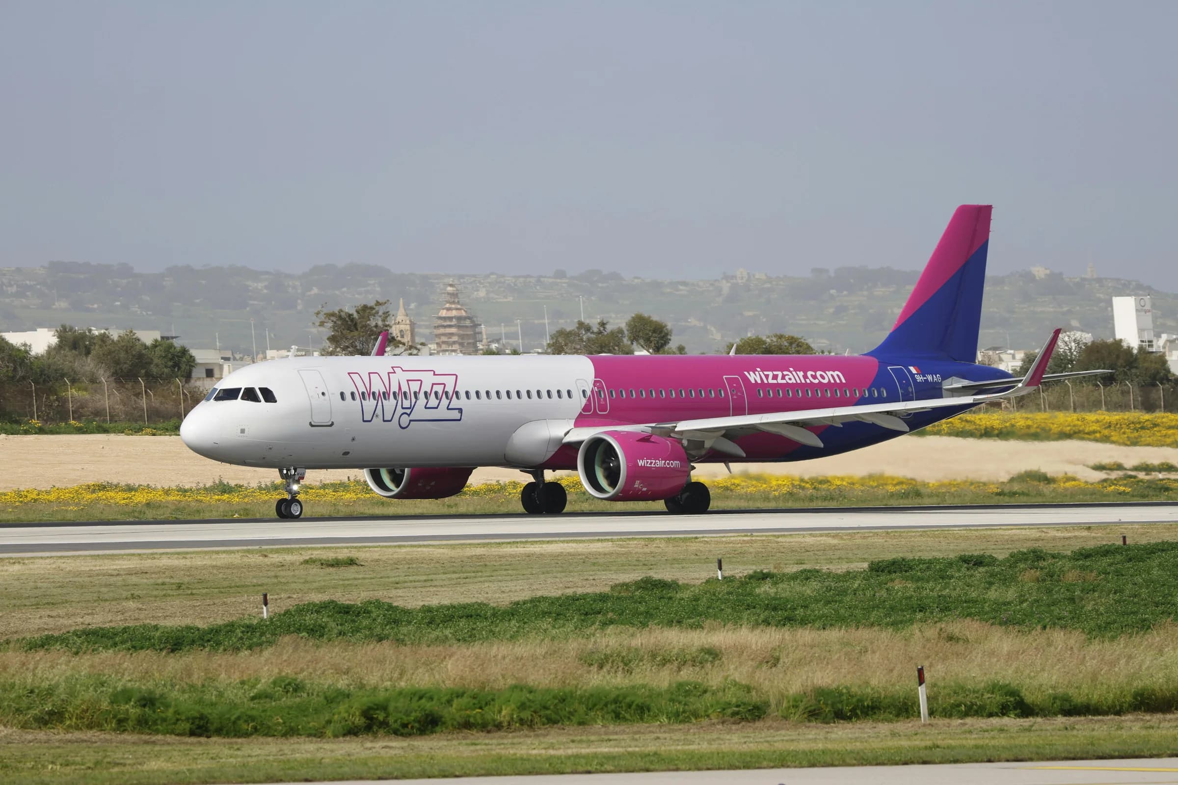 A Wizz Air Airbus A321 airplane taxis on the runway with a landscape background.