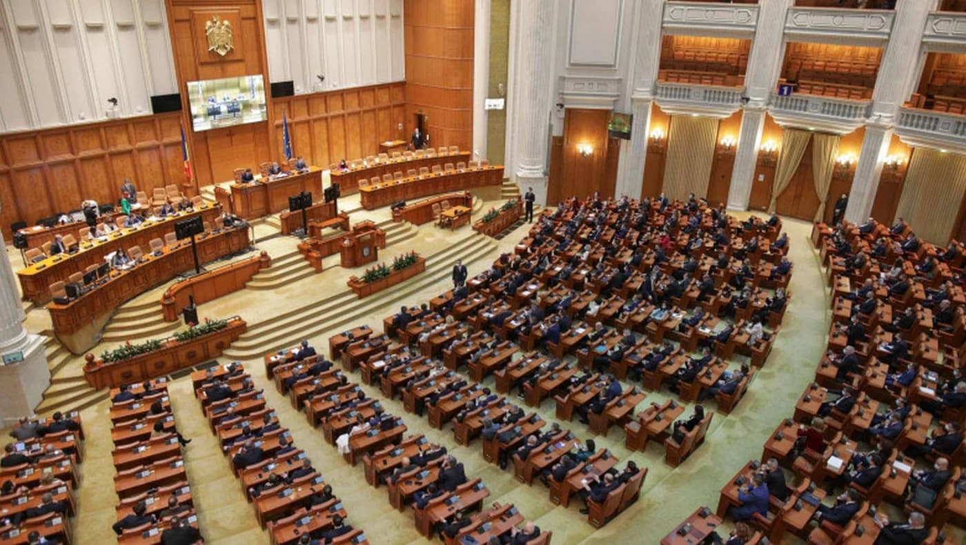 Vedere din plenul Parlamentului României cu parlamentari în hemiciclu, bănci legislative din lemn, tribune și arhitectură clasică a sălii de ședință legislativă.