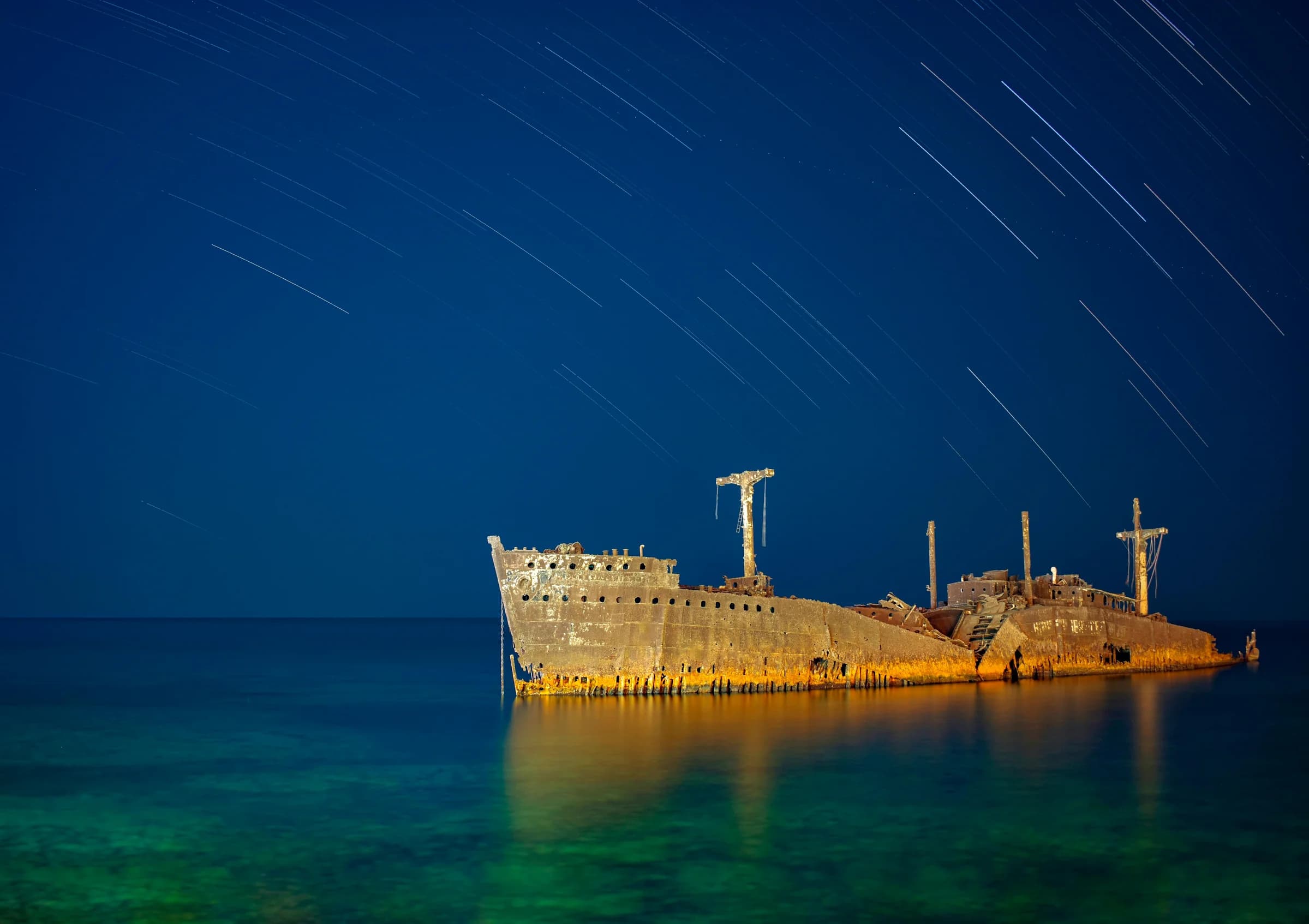 Dramatic capture of a shipwreck illuminated under a serene night sky with visible star trails.