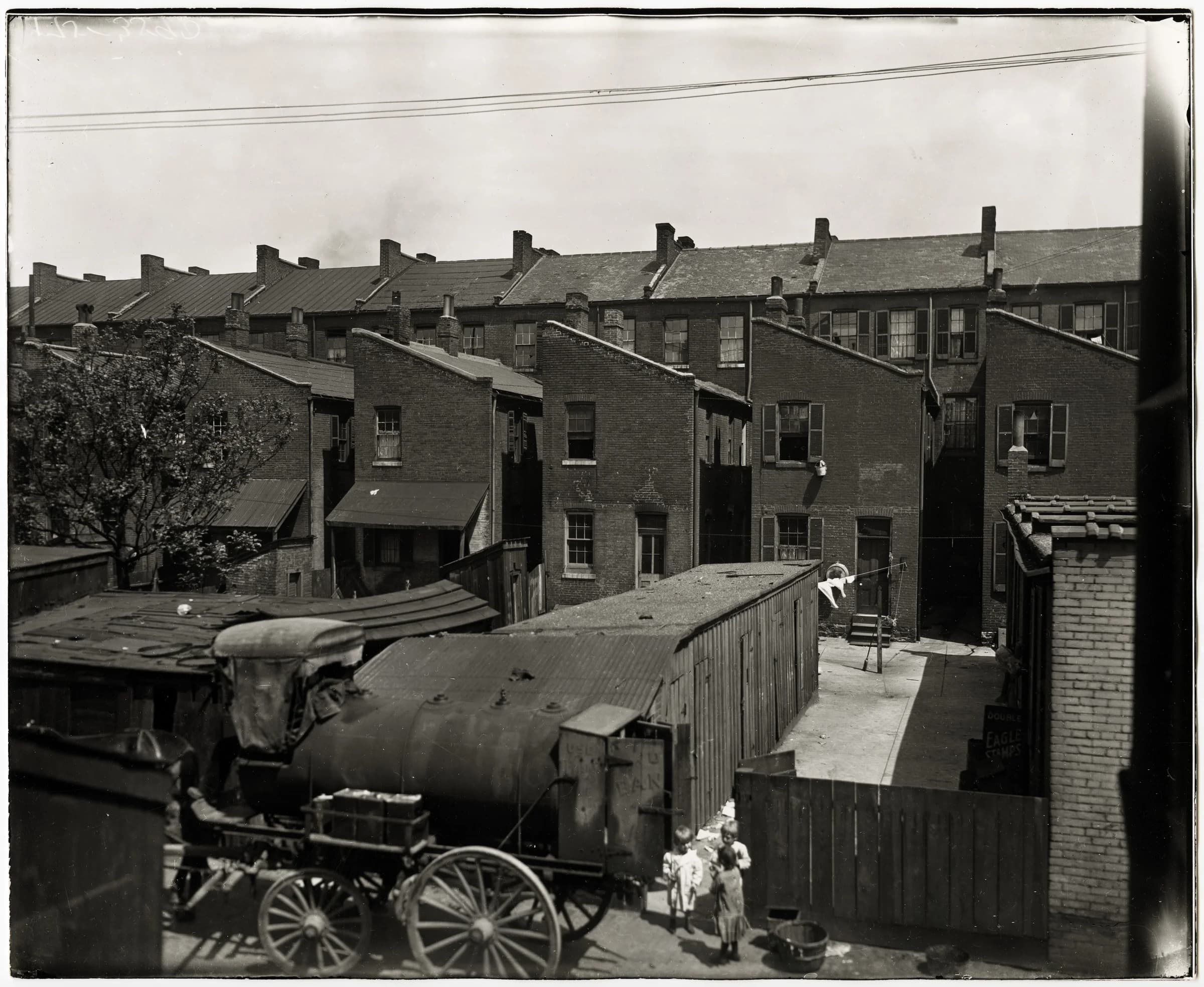 Children standing next to a tanker wagon in an unidentified alley behind row houses