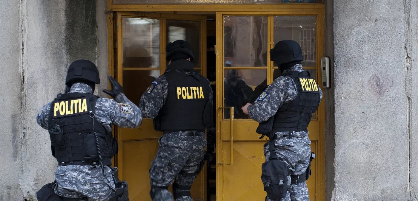 Ofițeri de poliție în echipament tactic efectuând control la o ușă; intervenție de aplicare a legii în context administrativ.