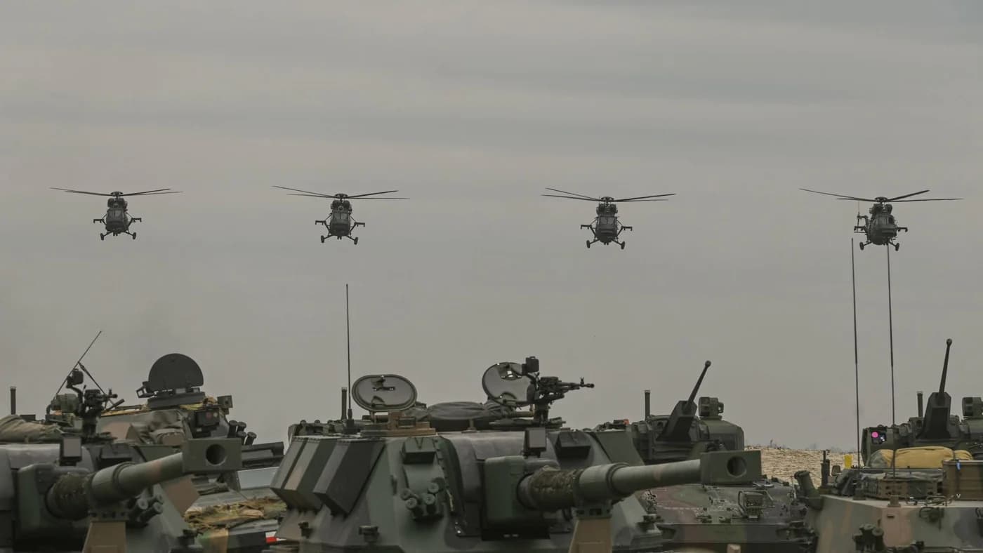 Patru elicoptere militari în formație deasupra unui convoi de vehicule blindate și tunuri de artilerie, ilustrând exercițiile comune ale forțelor militare sud-coreene, japoneze și americane.