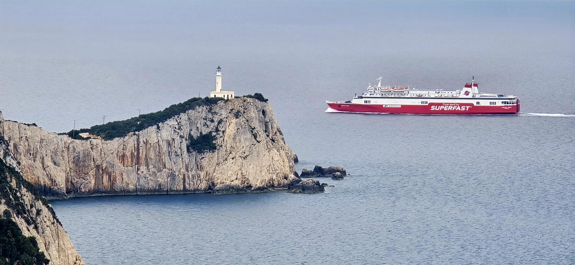 Feribotul SuperFast traversează strâmtoarea prin fața farului de la Cape Lefkatas, sudul insulei Lefkada, cu stânca albă verticală în prim plan