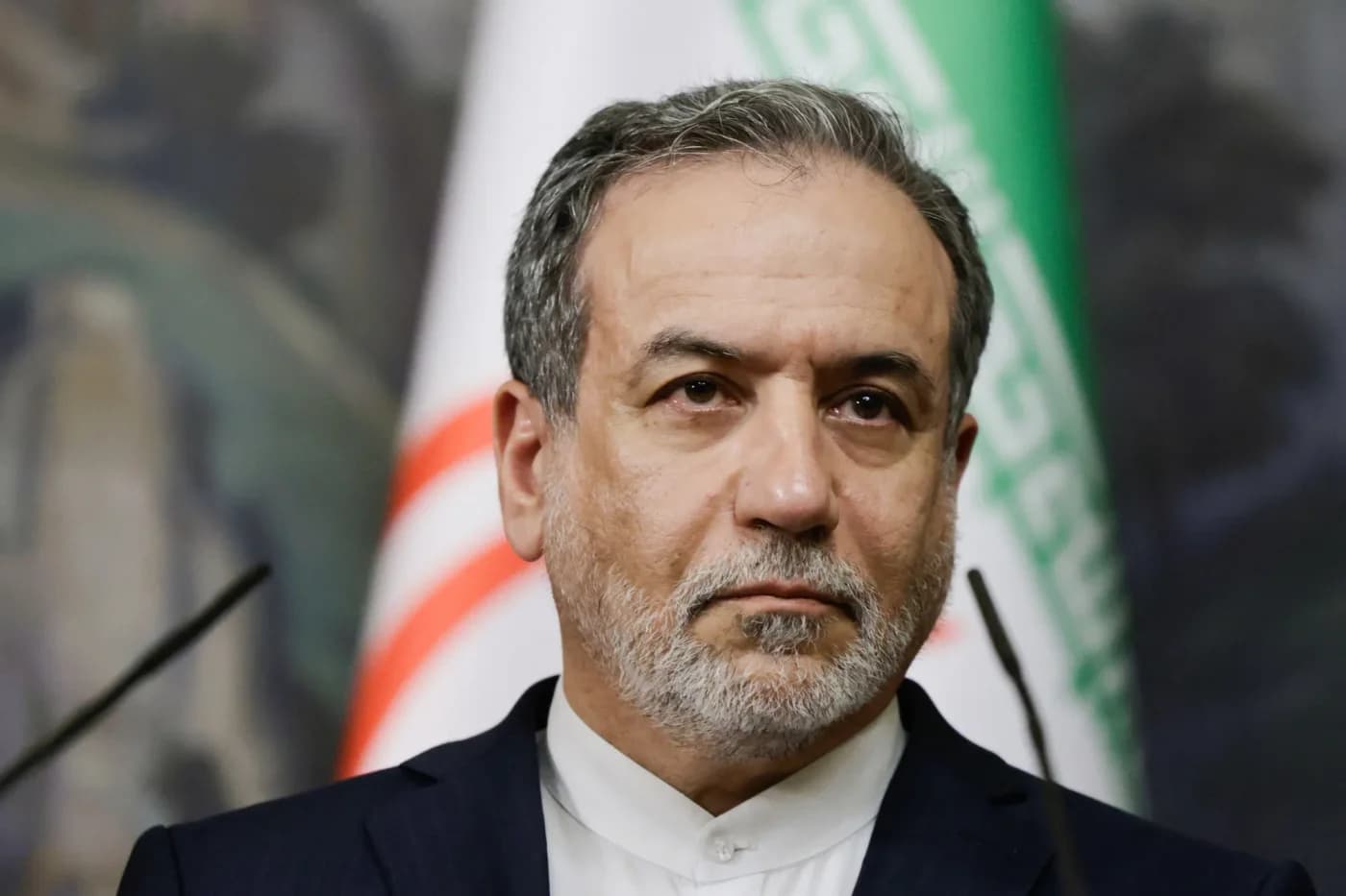Oficial iranian de înalt rang, în costum formal negru și cămașă albă, în fața drapeliei iraniene, cu expresie serioasă în contextul unei declarații diplomatice privind sancțiunile americane.