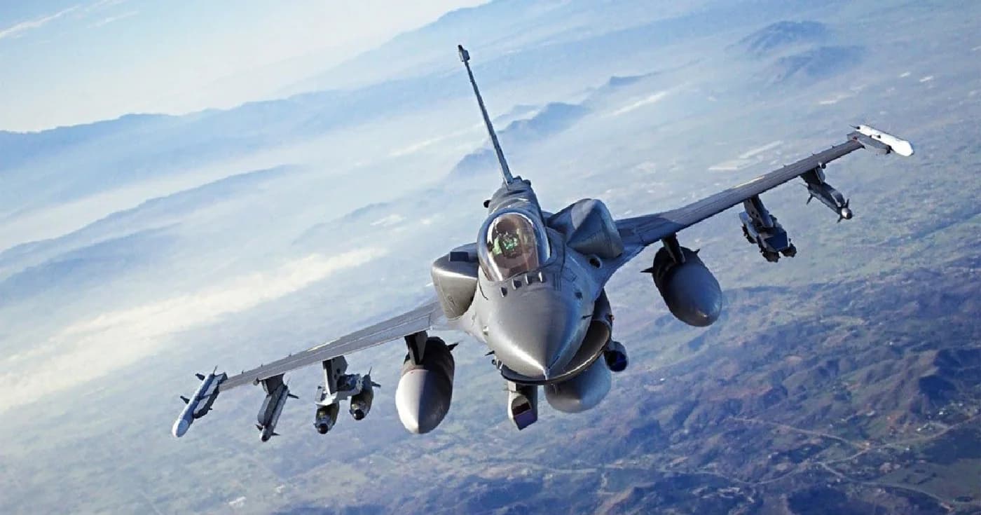 Formație de cinci avioane de luptă F-16 zburând deasupra unui teren muntos, cu armament extern atasat sub aripi și fuselaj, într-o misiune aeriană de antrenament sau patrulare.