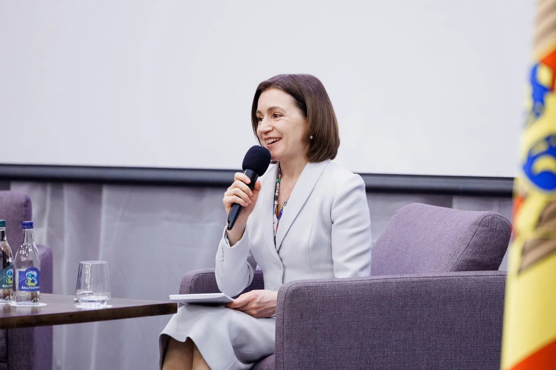 Maia Sandu, președinta Republicii Moldova, vorbind la microfon, cu drapelul moldovean în fundal