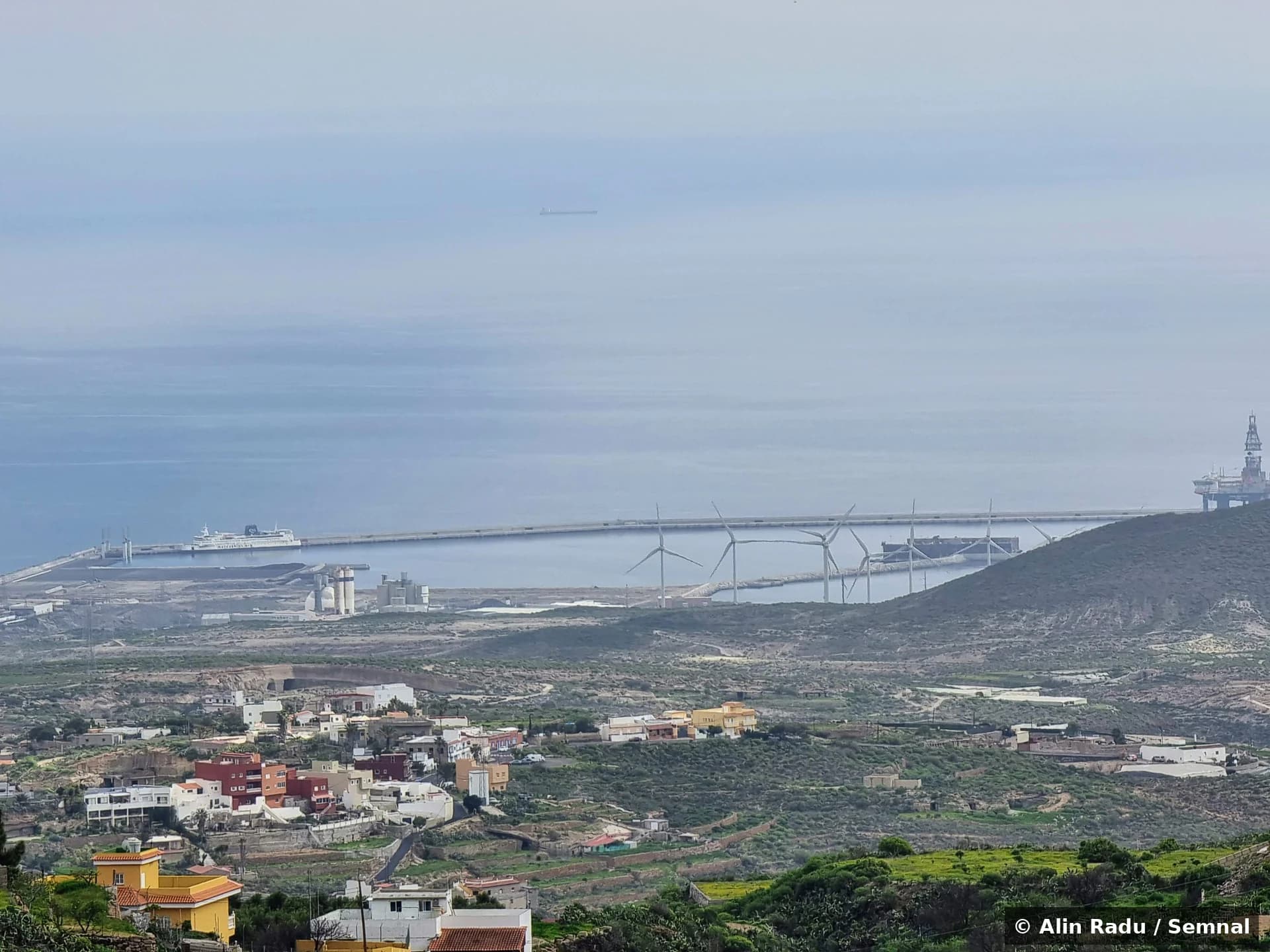 Vedere din înălțime asupra portului industrial Granadilla din sudul insulei Tenerife. În prim-plan, satul Granadilla de Abona; în fundal, portul cu turbine eoliene, vas mare ancorat la cheu și o platformă petroliferă în dreapta