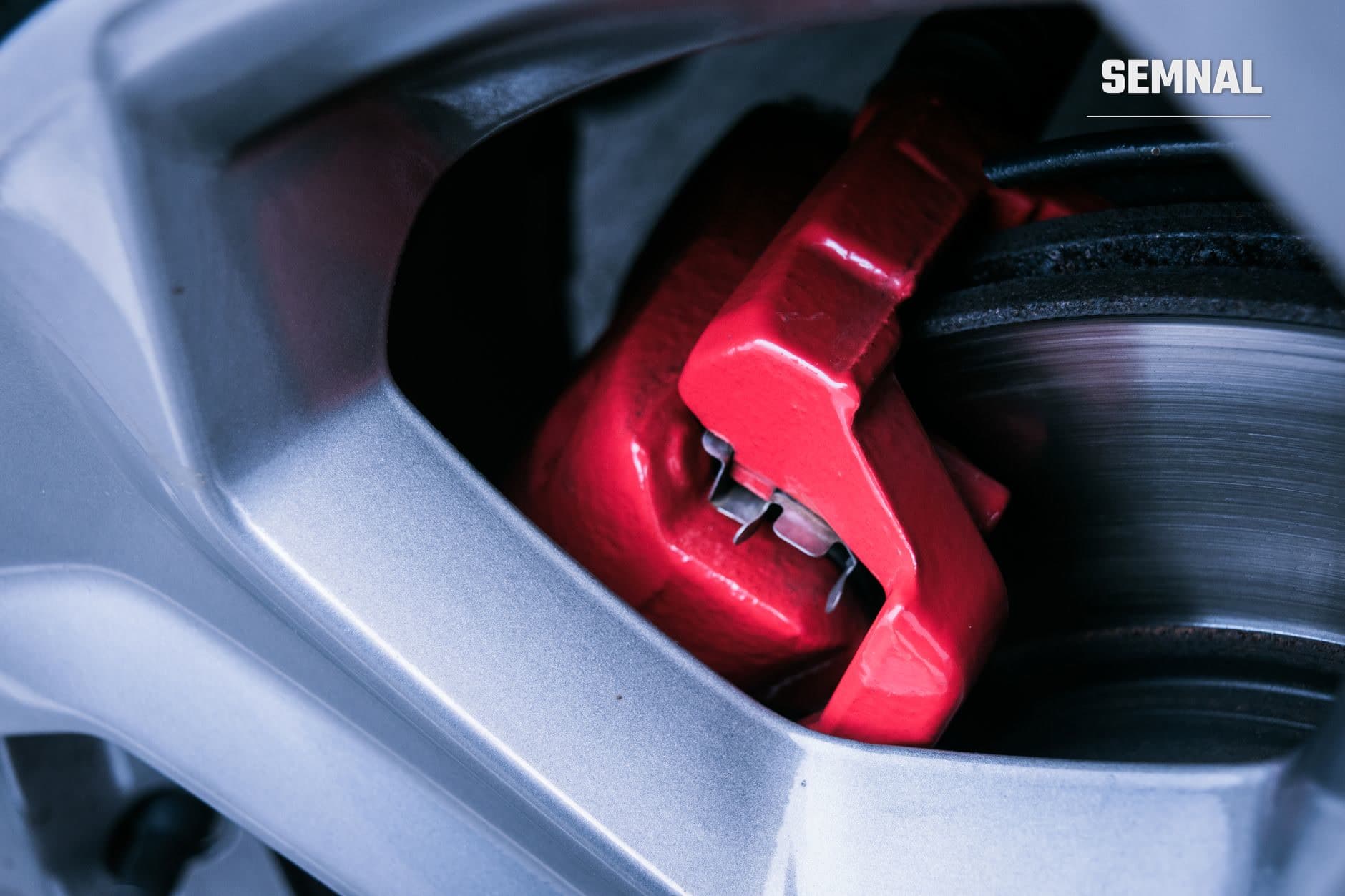 Detaliu al sistemului de frânare cu caliper roșu și disc de frânare negru pe roată de automobil, component esențială a sistemului ABS și ESP.