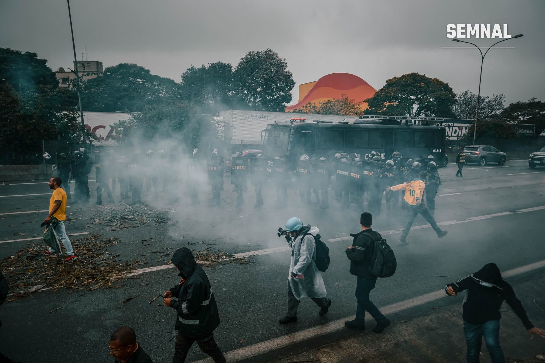 Forțe de poliție lansând gaz lacrimogen în fața manifestanților la Ceuta, manifestanți dispersați în fum gri, scene de confruntare directă cu protestatarii anti-migrație și agenții de ordine.