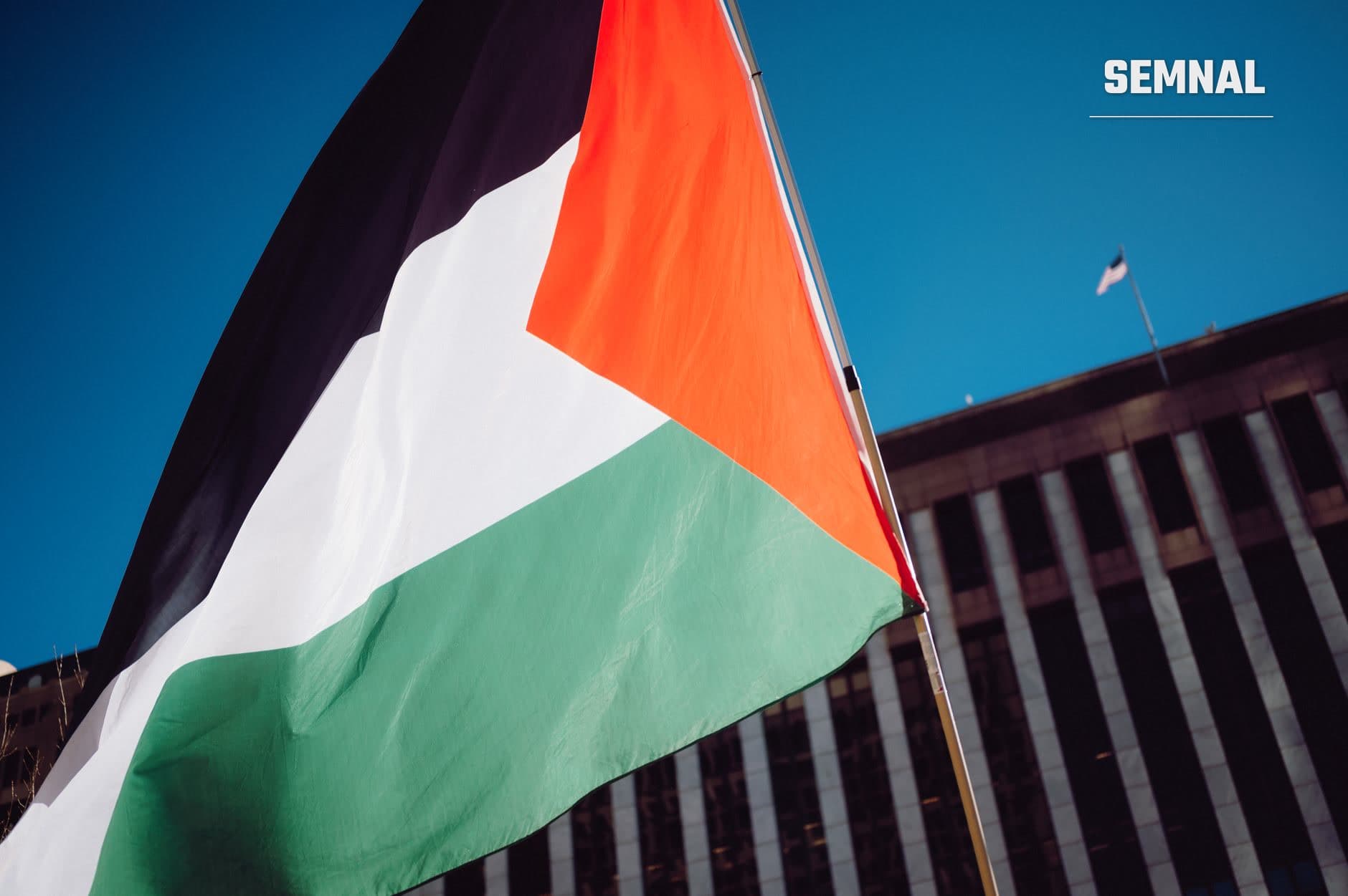 Steagul Palestinei plutind pe vânt în fata unei clădiri officiale, pe fundal albastru clar, reprezentând subiectele legate de relațiile diplomatice și petițiile adresate guvernelor occidentale. (Foto: Alfo Medeiros / Pexels)