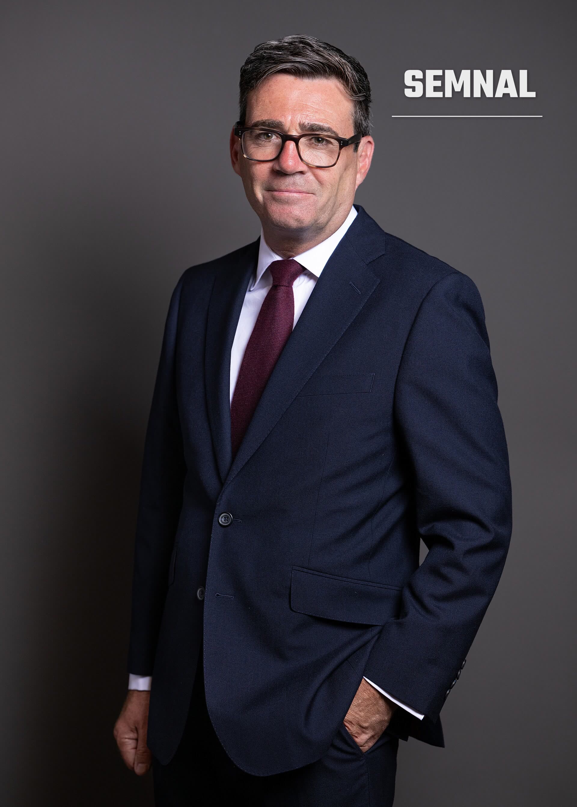 Andy Burnham, portret profesional în costum albastru și cravată burgundă, cu ochelari, pe fundal gri. (Foto: House of Commons)