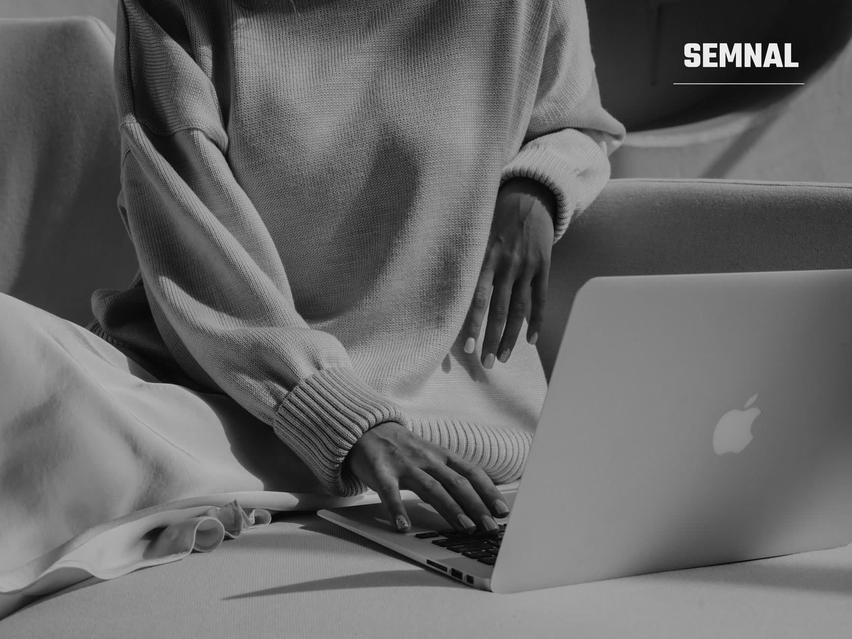 Persoană în pulover gri lucrând concentrat la un laptop pe birou alb, mâinile pe tastă în poziție de lucru activ. (Foto: Nadin Sh / Pexels)