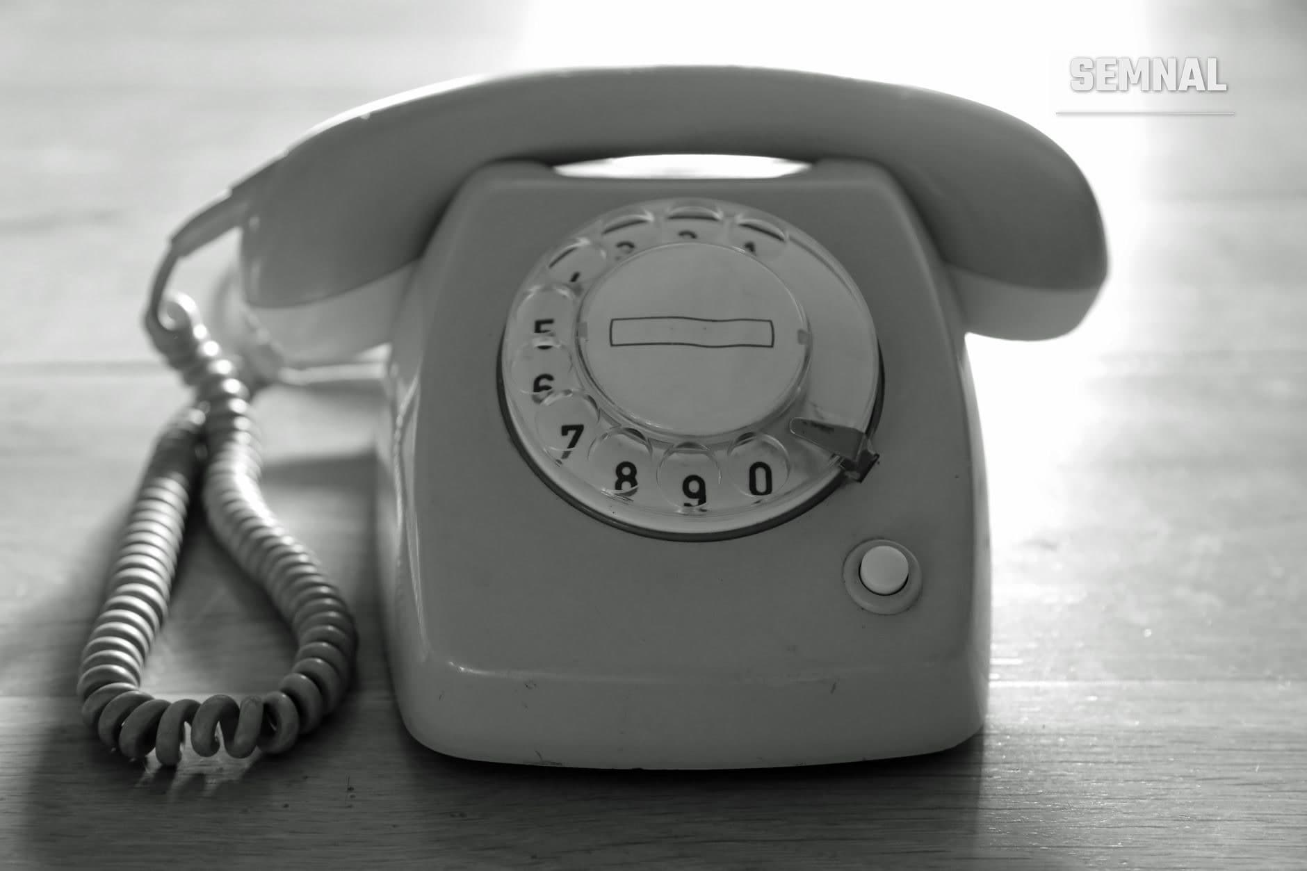 Telefon rotativ vintage alb-negru din perioada 1970-1980, cu receptor pe cordon spiralat și cadran numeric, pe fundal de lemn (Foto: Petra Ryan / Pexels)