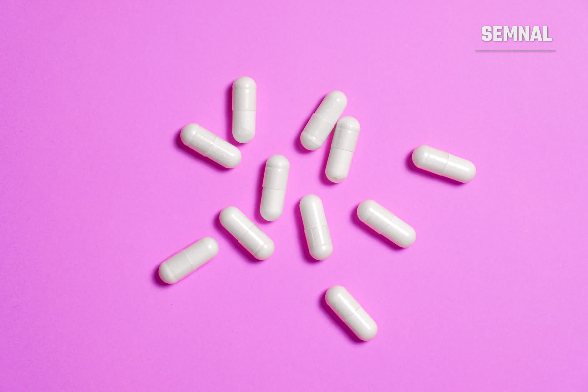 Unsprezece capsule albe de medicamente dispuse pe fundal roz, reprezentând conceptul de efect placebo și influența psihologică asupra percepției durerii și recuperării. (Foto: Anna Shvets / Pexels)