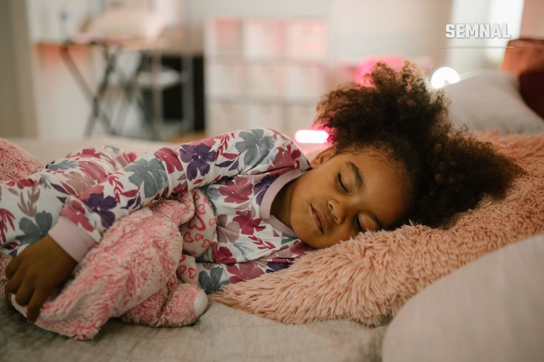 Copilă care doarme pașnic pe un pat, îmbrăcată în pijamale cu modele florale, într-o cameră cu iluminare moale și liniștitoare. (Foto: RDNE Stock project / Pexels)