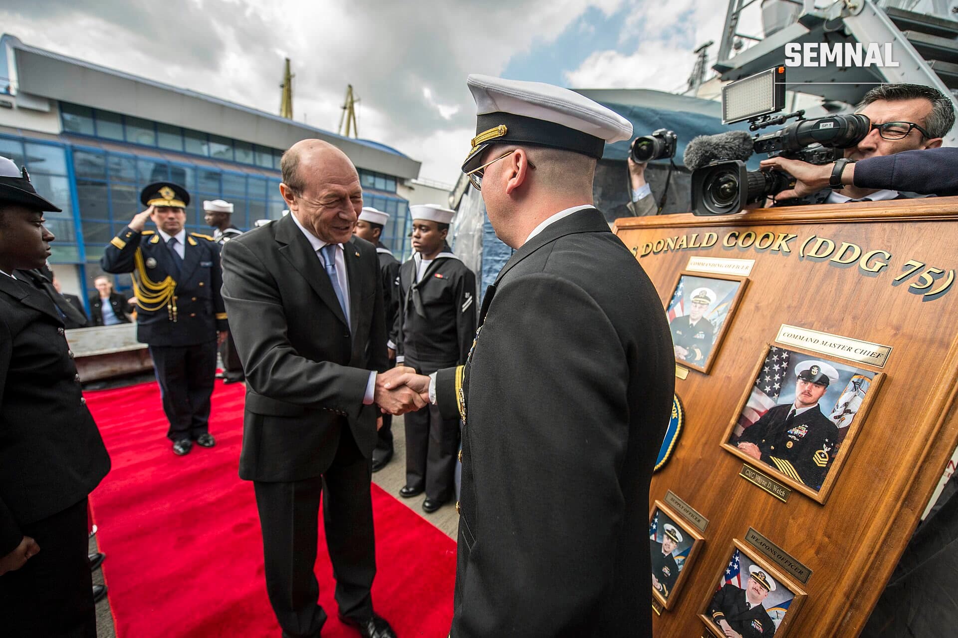 Traian Băsescu strângând mâna cu un ofițer naval în uniforme de gală, la un eveniment oficial pe o navă militară americană cu coborârea în prim-plan. (Foto: Official U.S. Navy Page from United States of America)