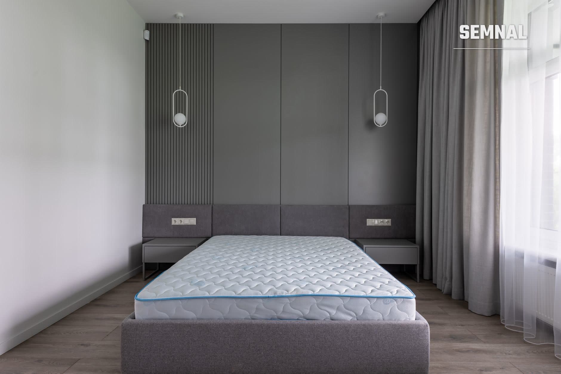 Dormitor modern cu o salteă albastră și albă exponată pe un pat tapițat gri, cu perete acoperit și draperii gri deschis. (Foto: Max Vakhtbovych / Pexels)