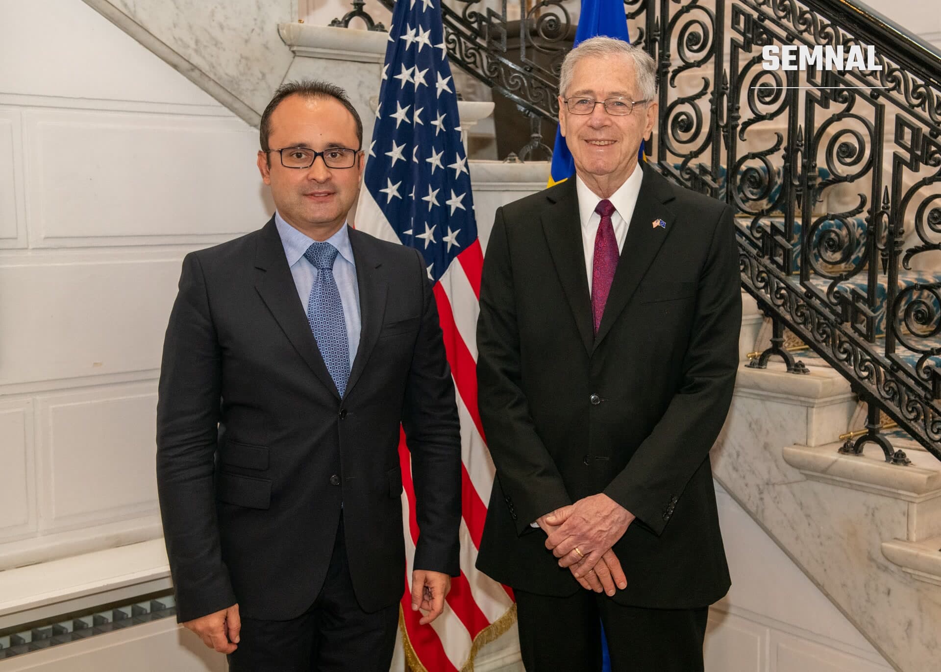 Cristian Bușoi, secretar de stat, la o întâlnire oficială în fața steagurilor SUA și Franței, alături de un oficial american în costum formal. (Foto: U.S. Mission to the European Union)