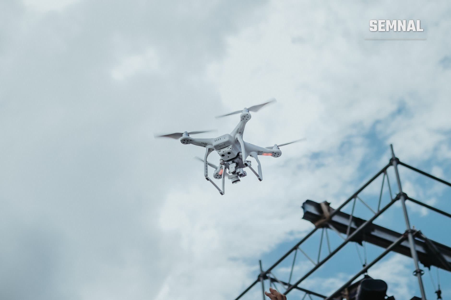 Dronă cu patru elice zburând în cer noros, fotografiată de jos cu un pilon electric parțial vizibil în fundal defocalizat. (Foto: Rodolfo Quirós / Pexels)