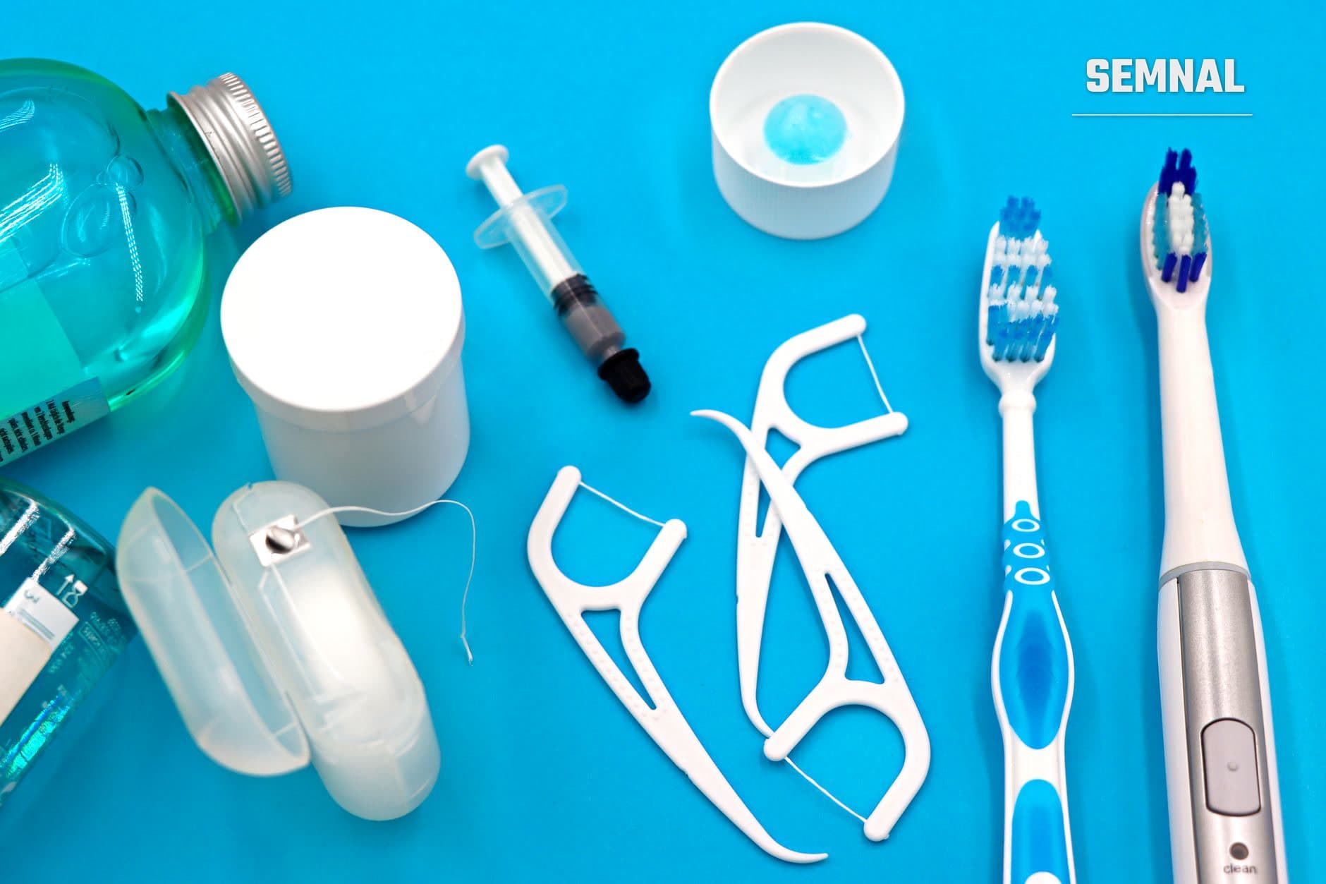 Colecție de instrumente și produse pentru igiena orală: apă de gură, flos, periuțe de dinți, gel dental și recipiente pe fundal albastru cian. (Foto: Marta Branco / Pexels)