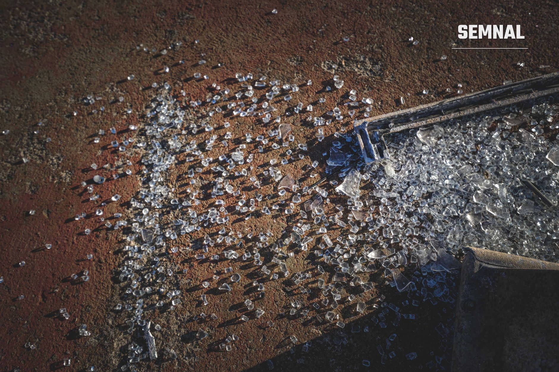 Fragmente metalice argintii și rămășițe dispersate pe pământ roșu-maro, lângă un recipient metalic albastru, ilustrând urmele unui impact de proiectil sau detunare. (Foto: Francesco Ungaro / Pexels)