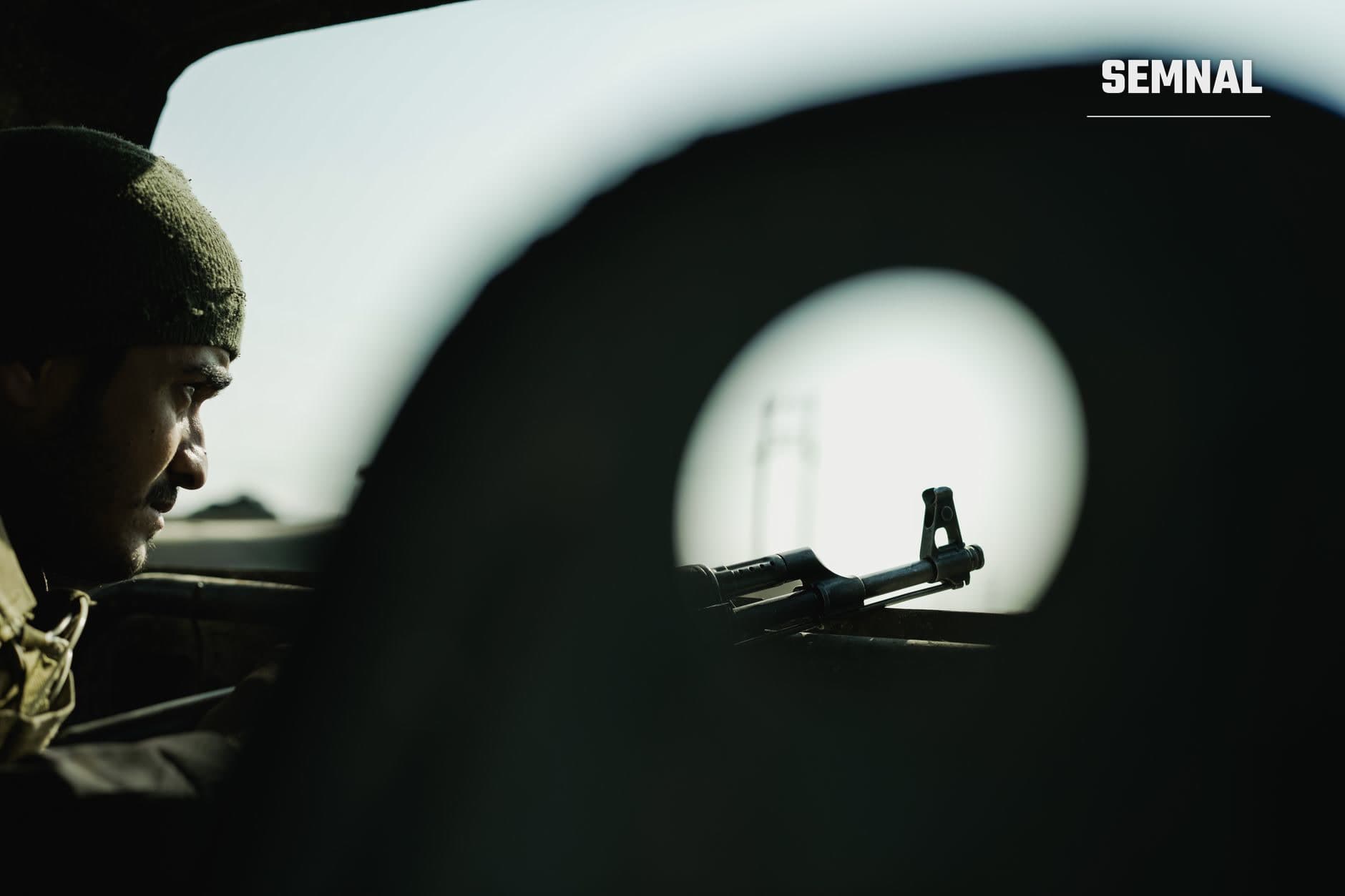 Militar în uniformă observă prin vizor optic o armă dotată cu telemetru, într-un mediu întuneric, cu lumina difuză în fundal. (Foto: AMORIE SAM / Pexels)