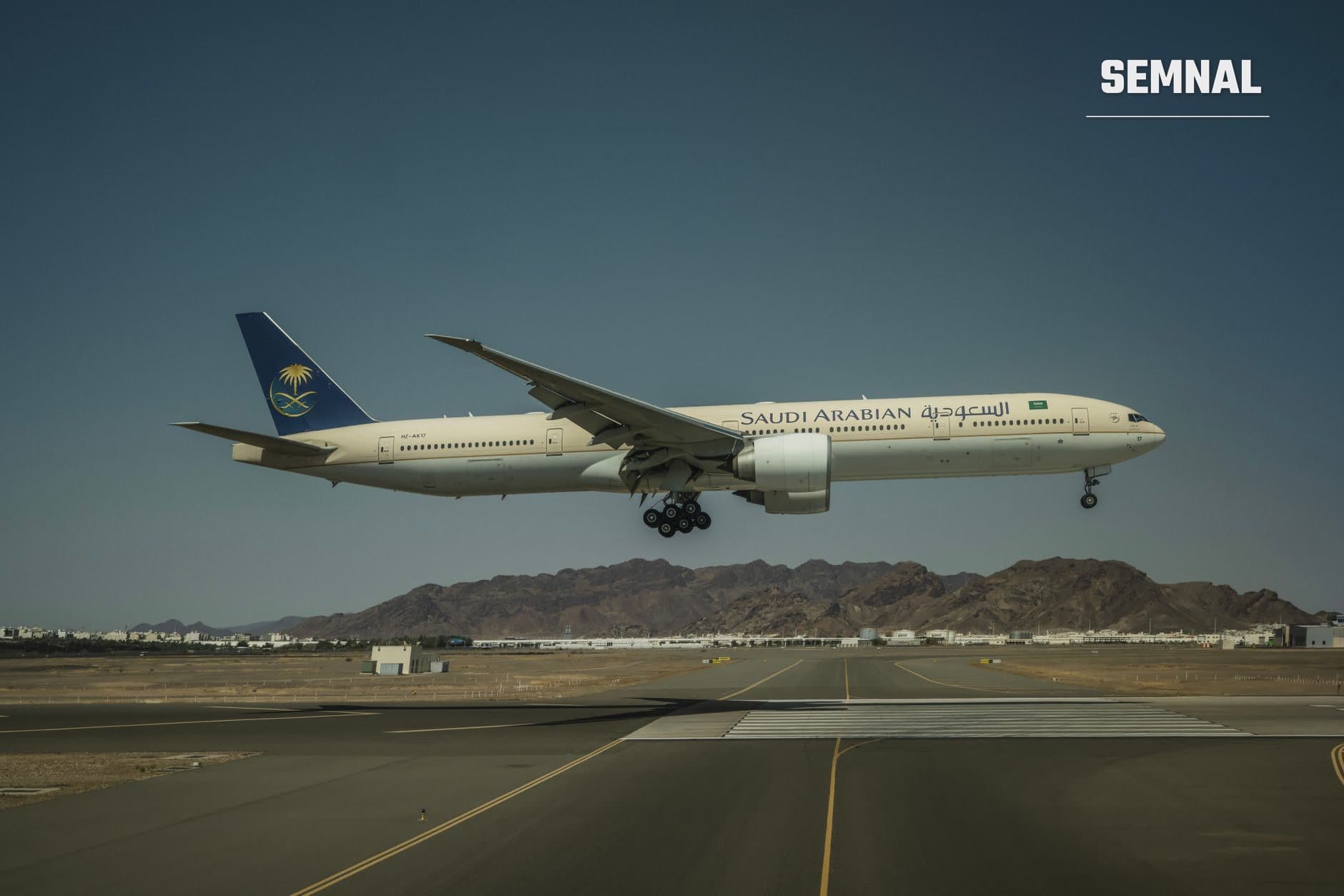 Avion Saudi Arabian Airlines aterizând pe pista aeroportului din Riad, cu munți arizi și clădiri de aeroport în fundal sub cer senin. (Foto: Miguel Cuenca / Pexels)