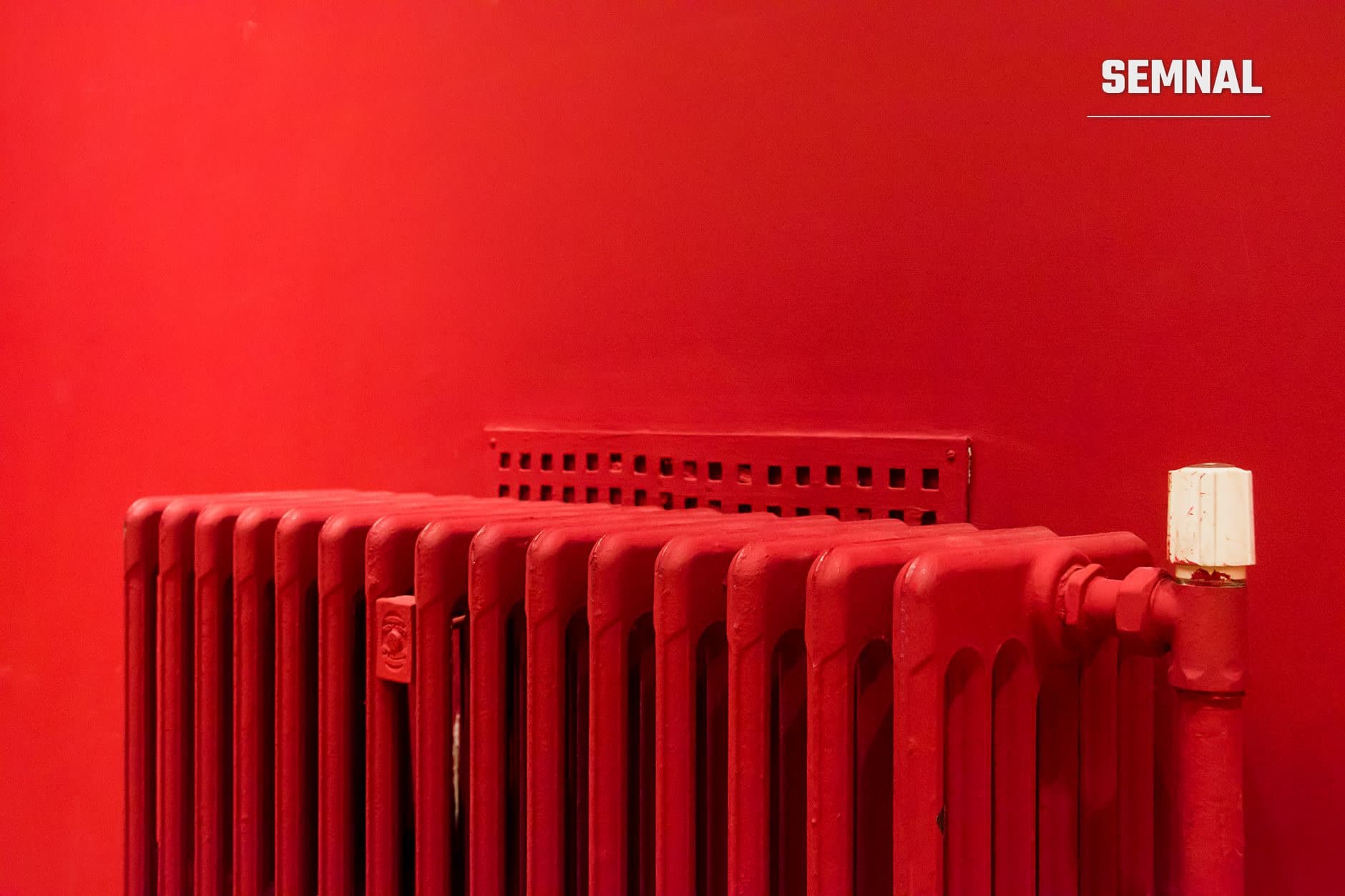 Radiator metalic roșu cu nervuri verticale pe perete roșu, cu grătar de ventilație și cutie de control albă, simbol al sistemelor de încălzire deficitare din blocurile anilor '80. (Foto: Jan van der Wolf / Pexels)