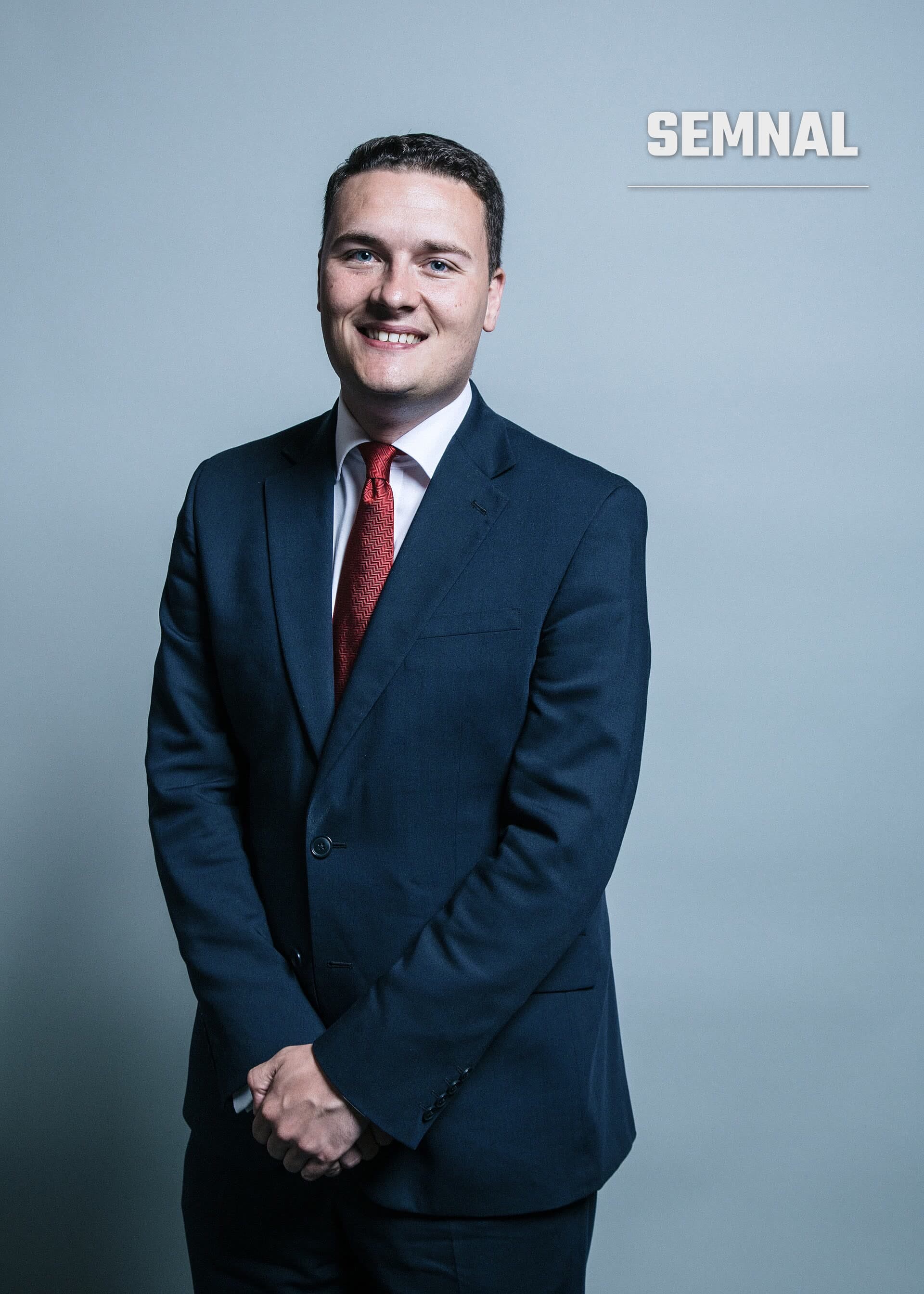 Wes Streeting, într-un costum bleumarin, cămașă albă și cravată roșie, zâmbind într-un portret pe fundal gri-albăstrui. (Foto: Chris McAndrew)